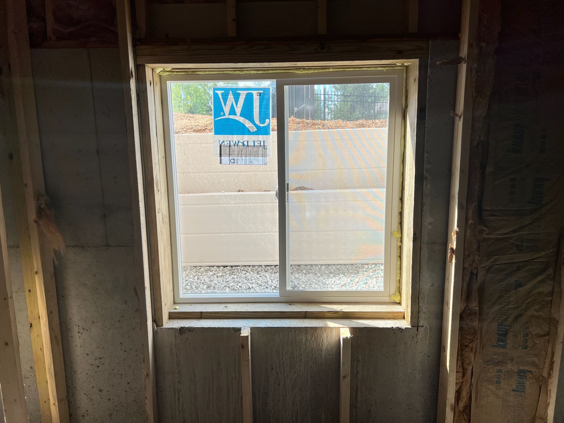 Window installed in a partially constructed wall with insulation, outside view of gravel and building materials.