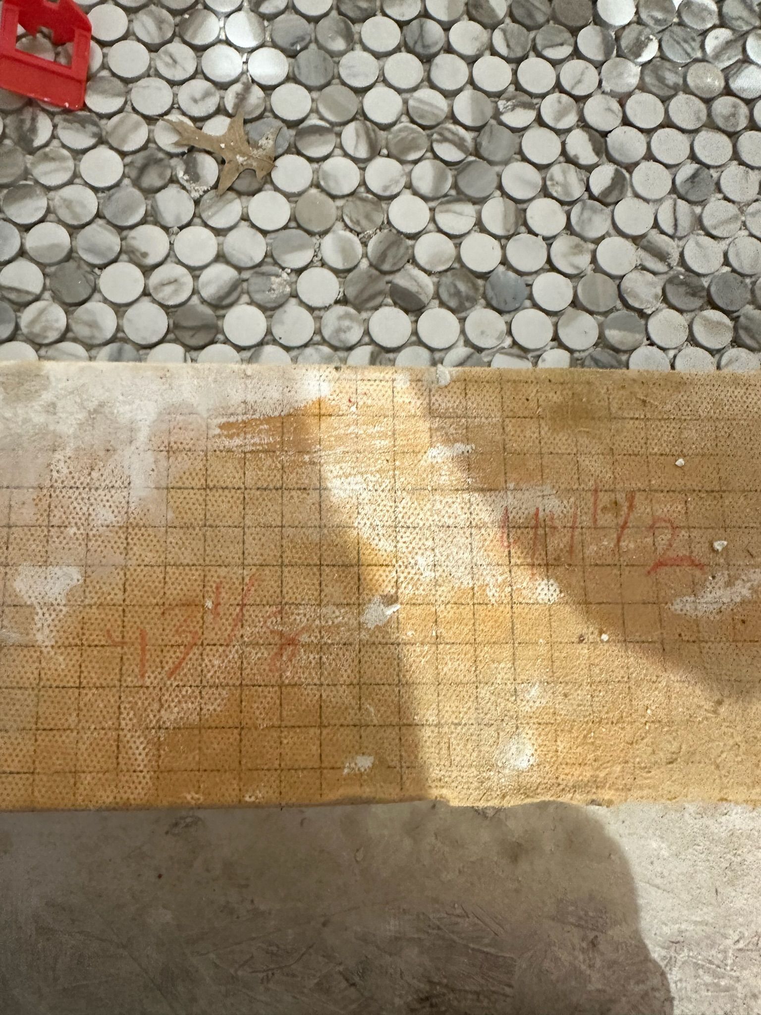 Close-up: mosaic tile installation in progress. Penny tile, marked plywood, and concrete surface.