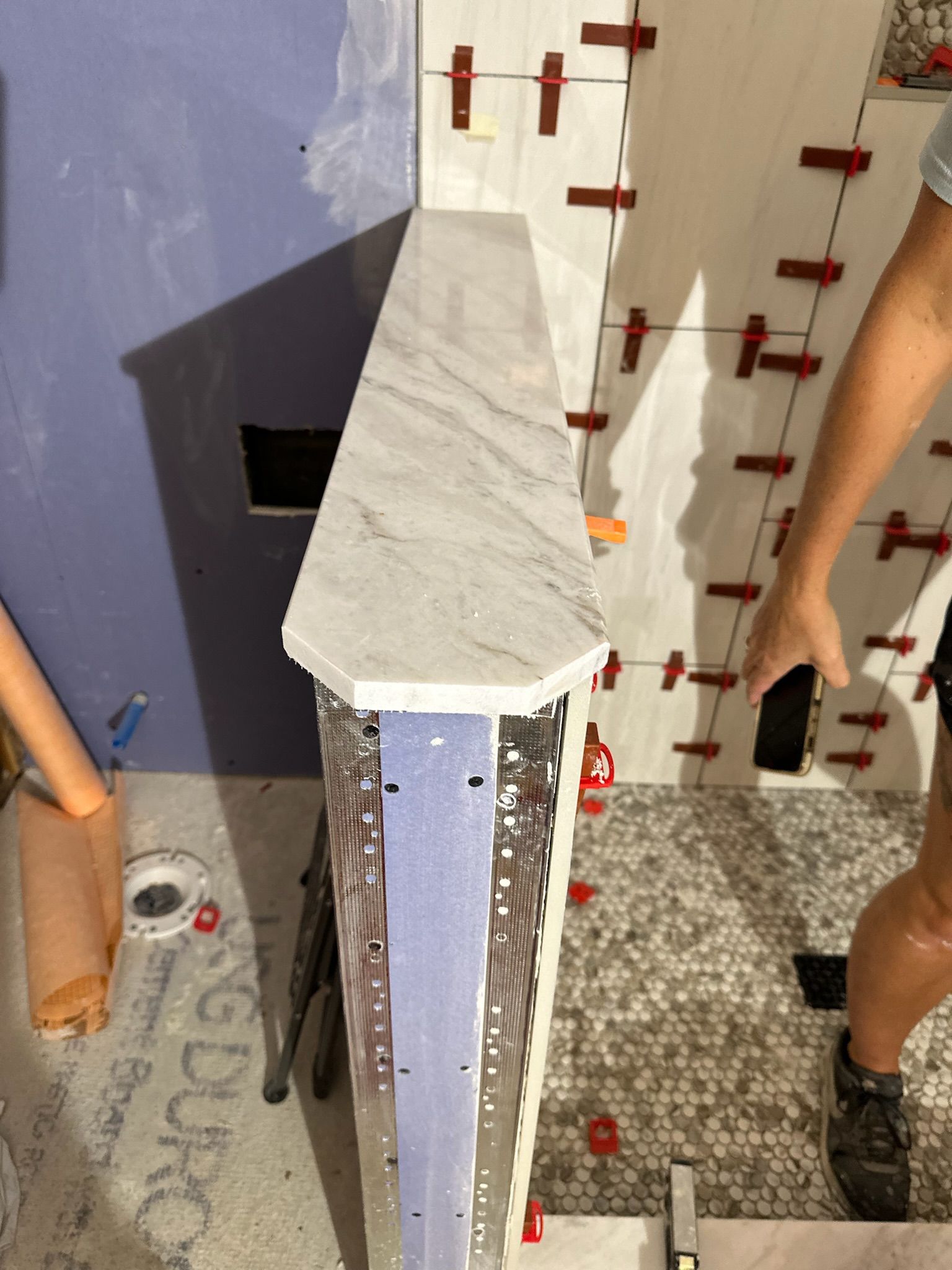 Shower niche construction with tile, marble shelf, and leveling clips.