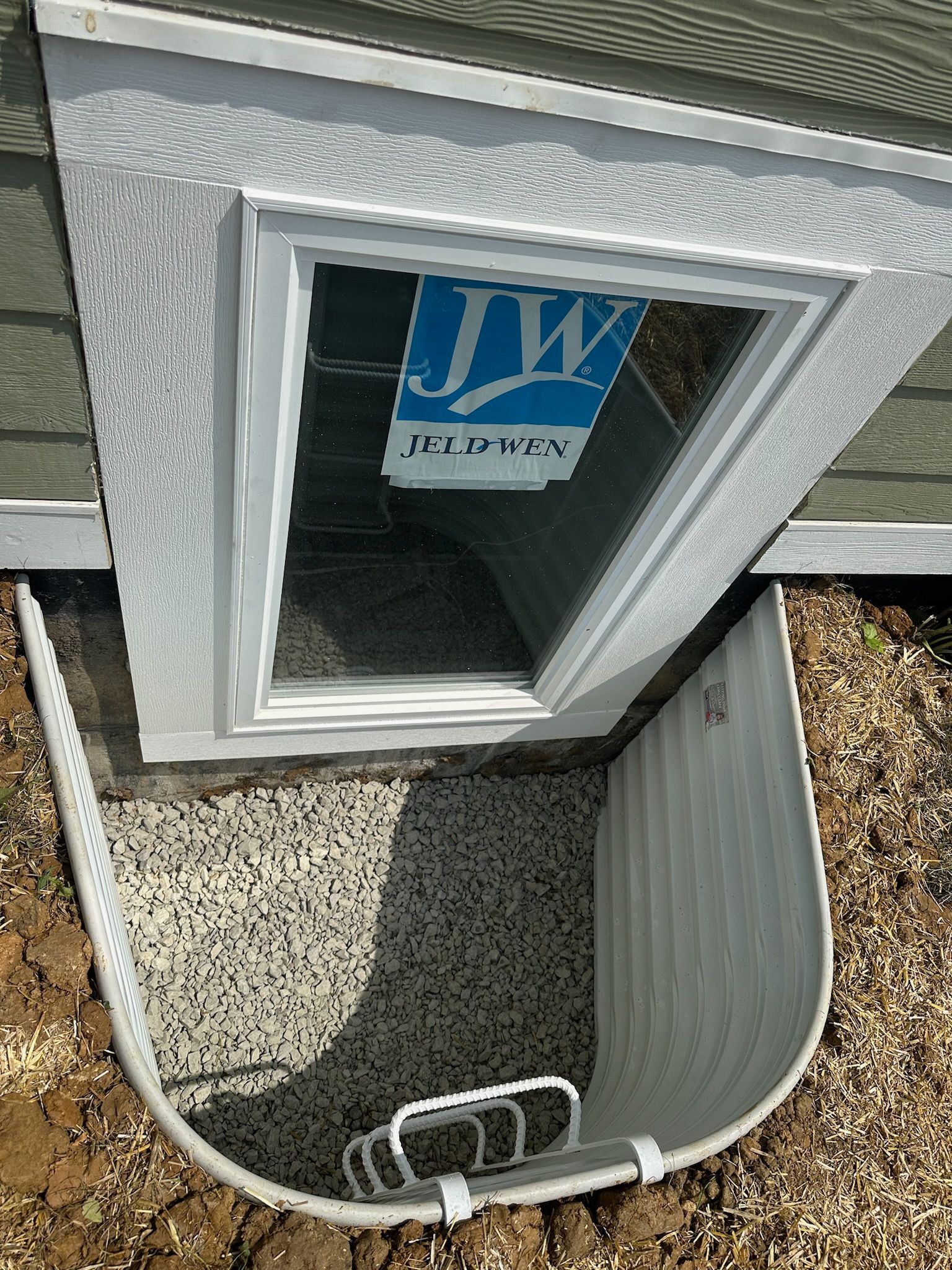 Basement window with a white window well and gravel.