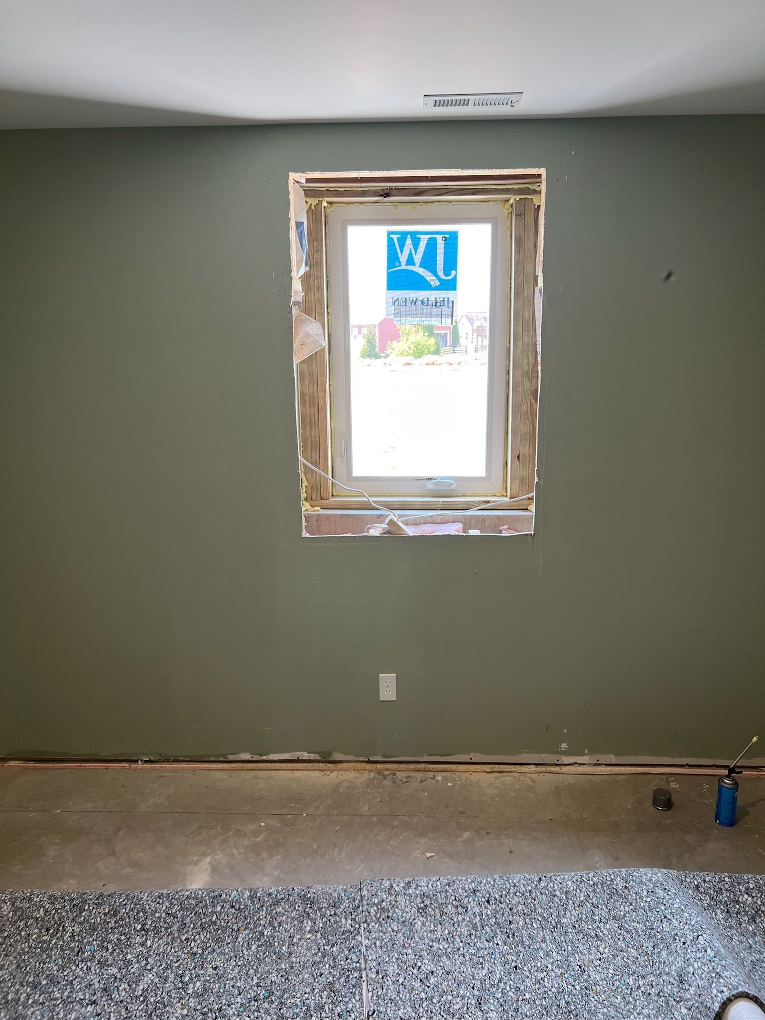 Room with a window, olive-green walls, and a cement floor under construction.