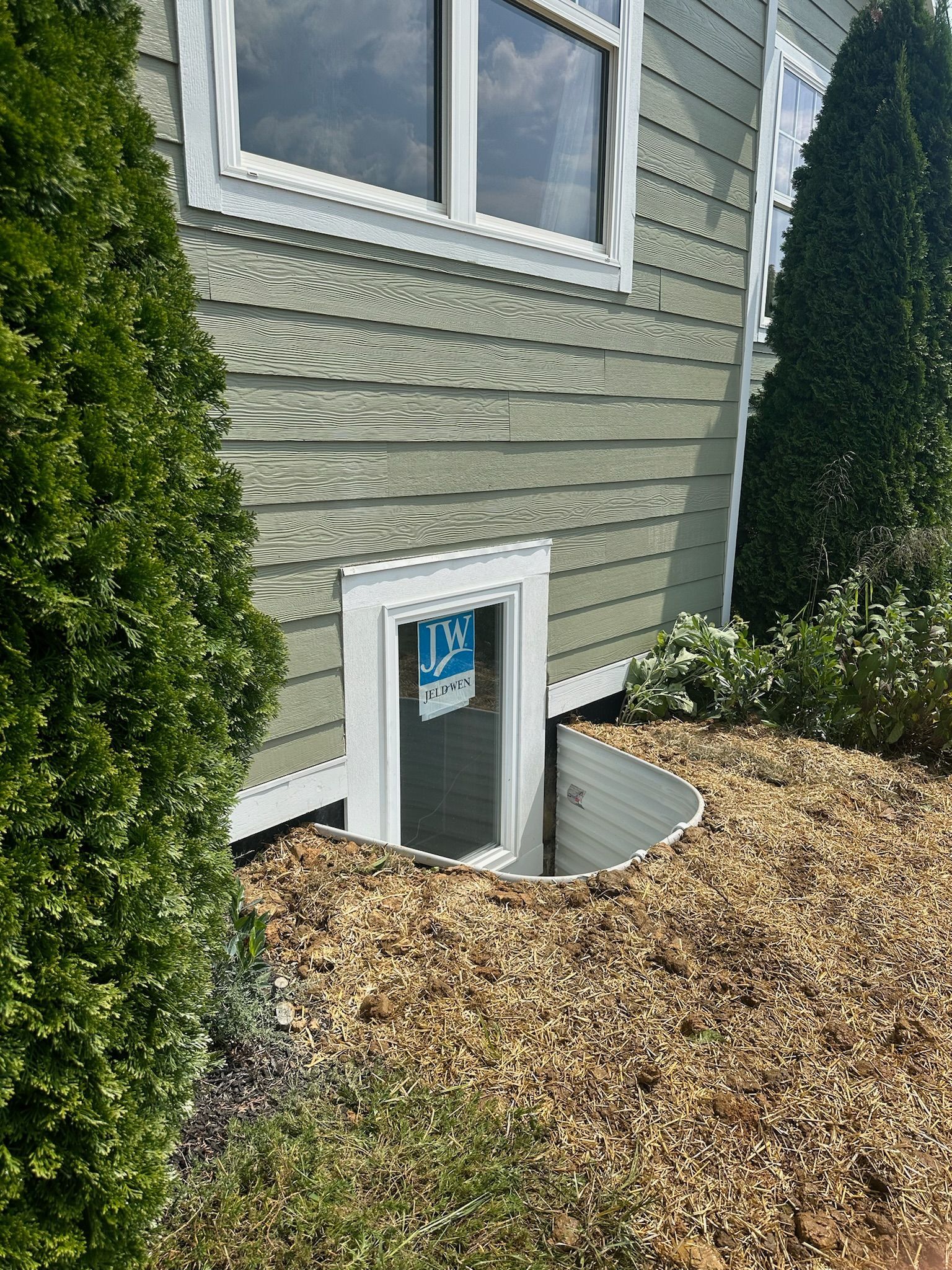 House exterior with a basement window surrounded by gravel and shrubbery.