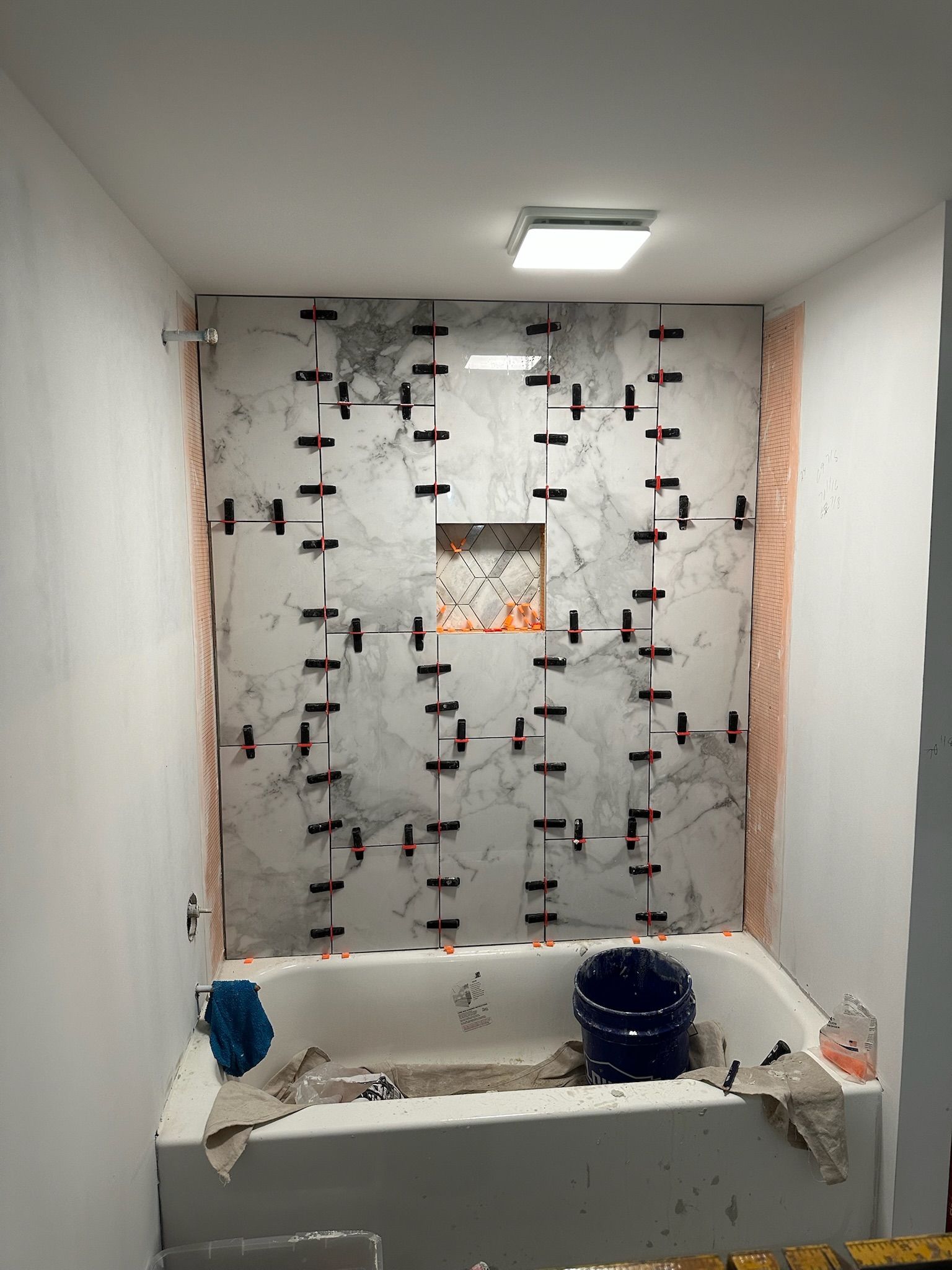 Bathroom with marble-look tile in progress, tub, niche, and tile leveling spacers.