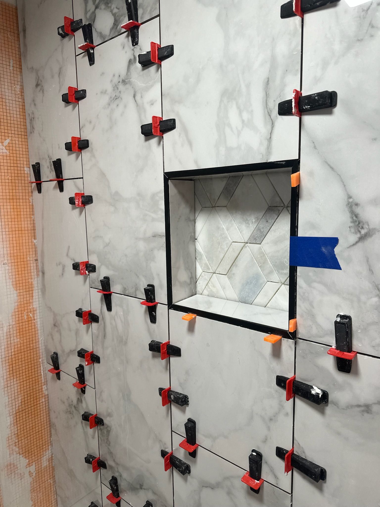 White marble tiles being installed with leveling system in a shower, with a built-in niche.