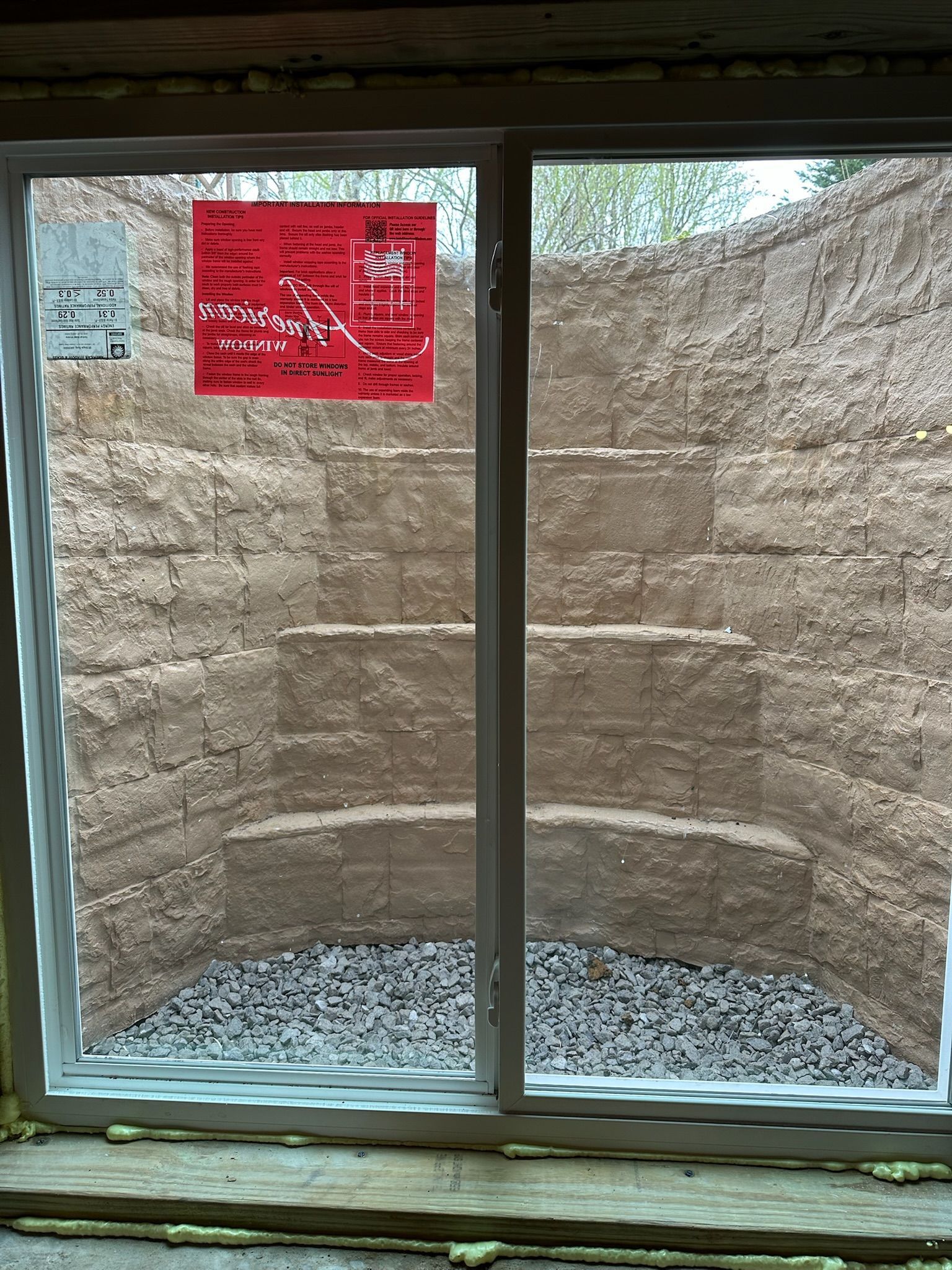 Window looking out at a tiered retaining wall made of stacked blocks; gravel at bottom.