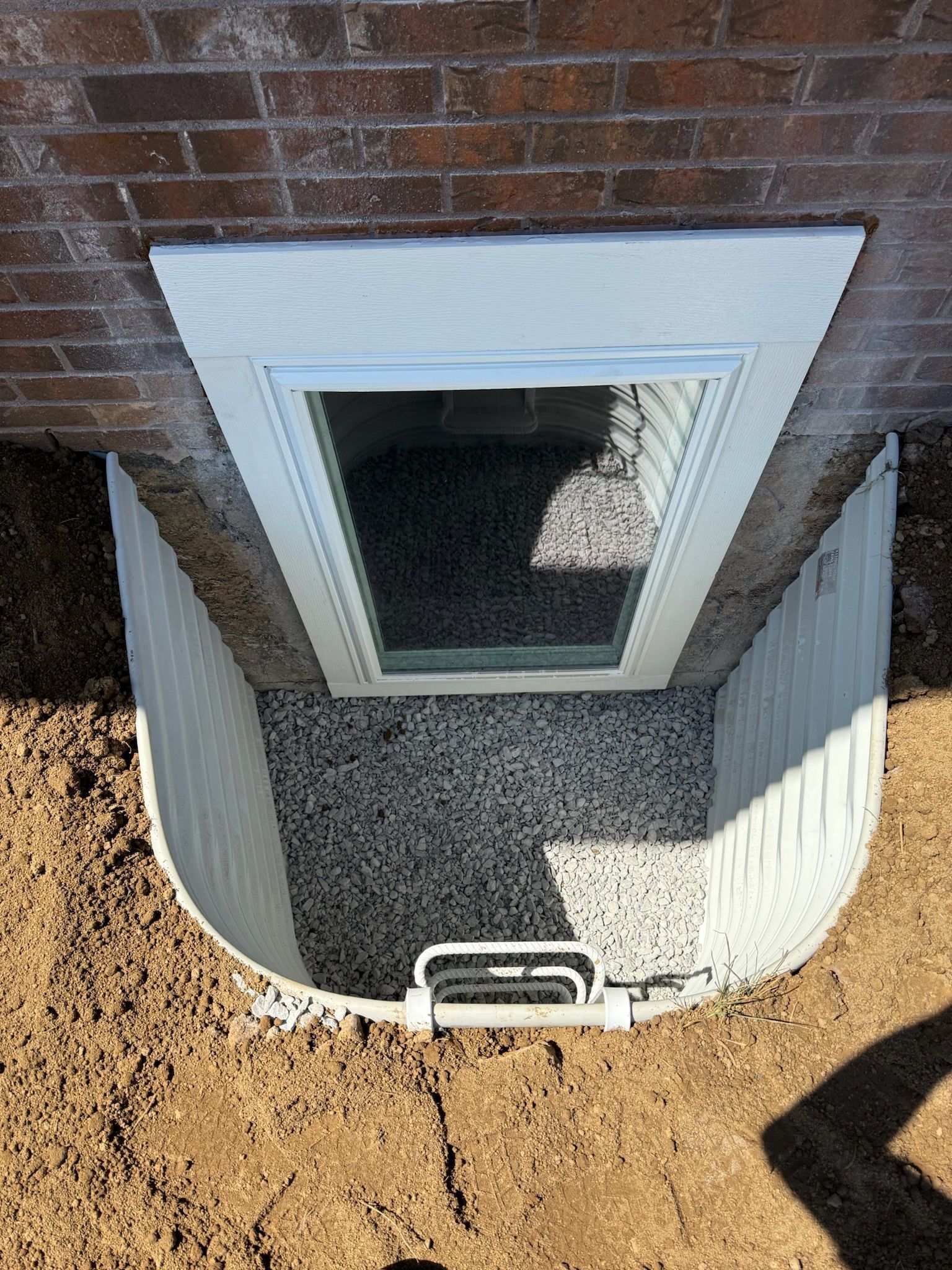 Basement window well with a window and gravel. White well against a brick wall.