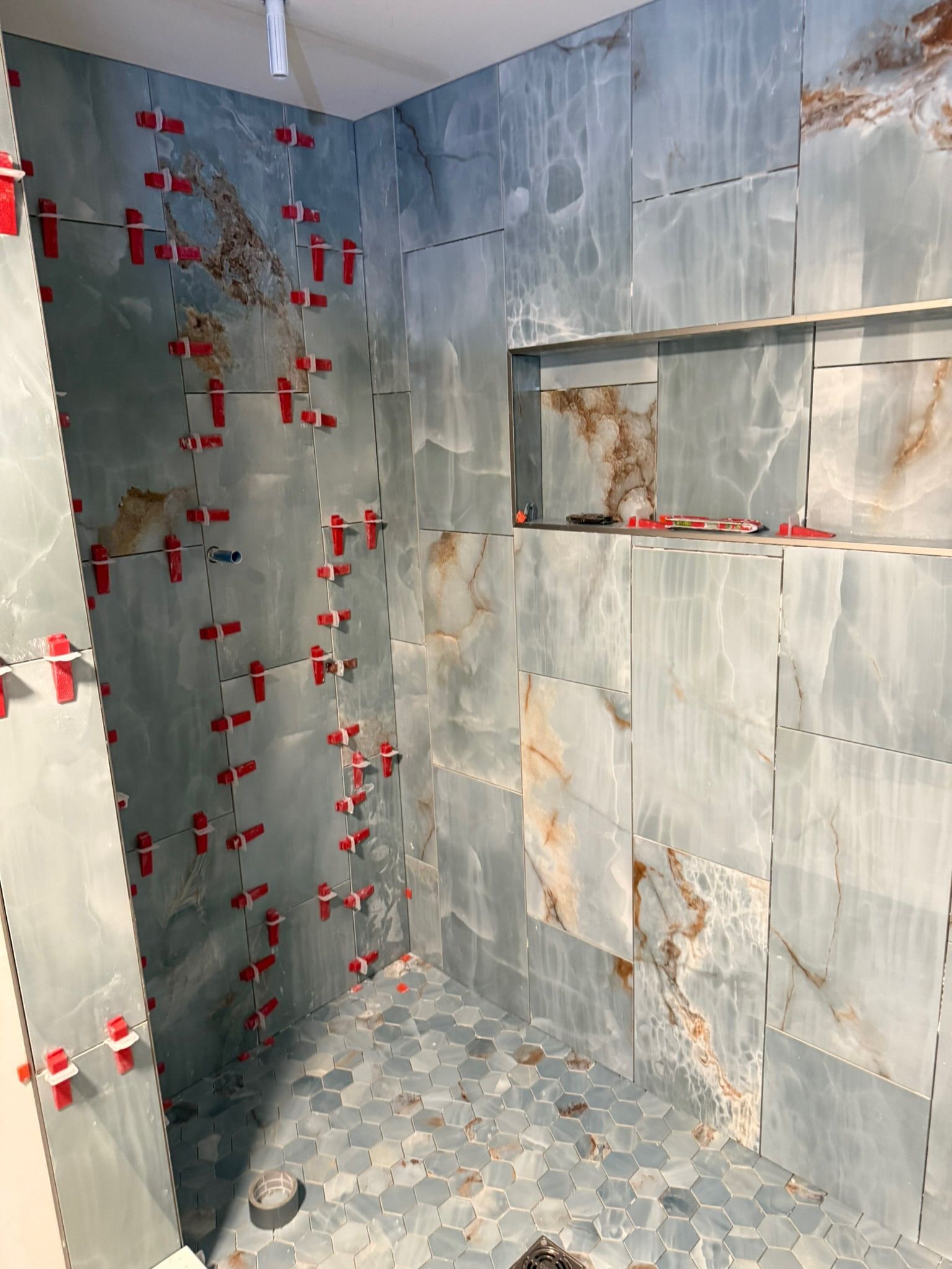 Shower stall under construction, blue-gray tile with stone-like patterns. Red tile spacers are in use.