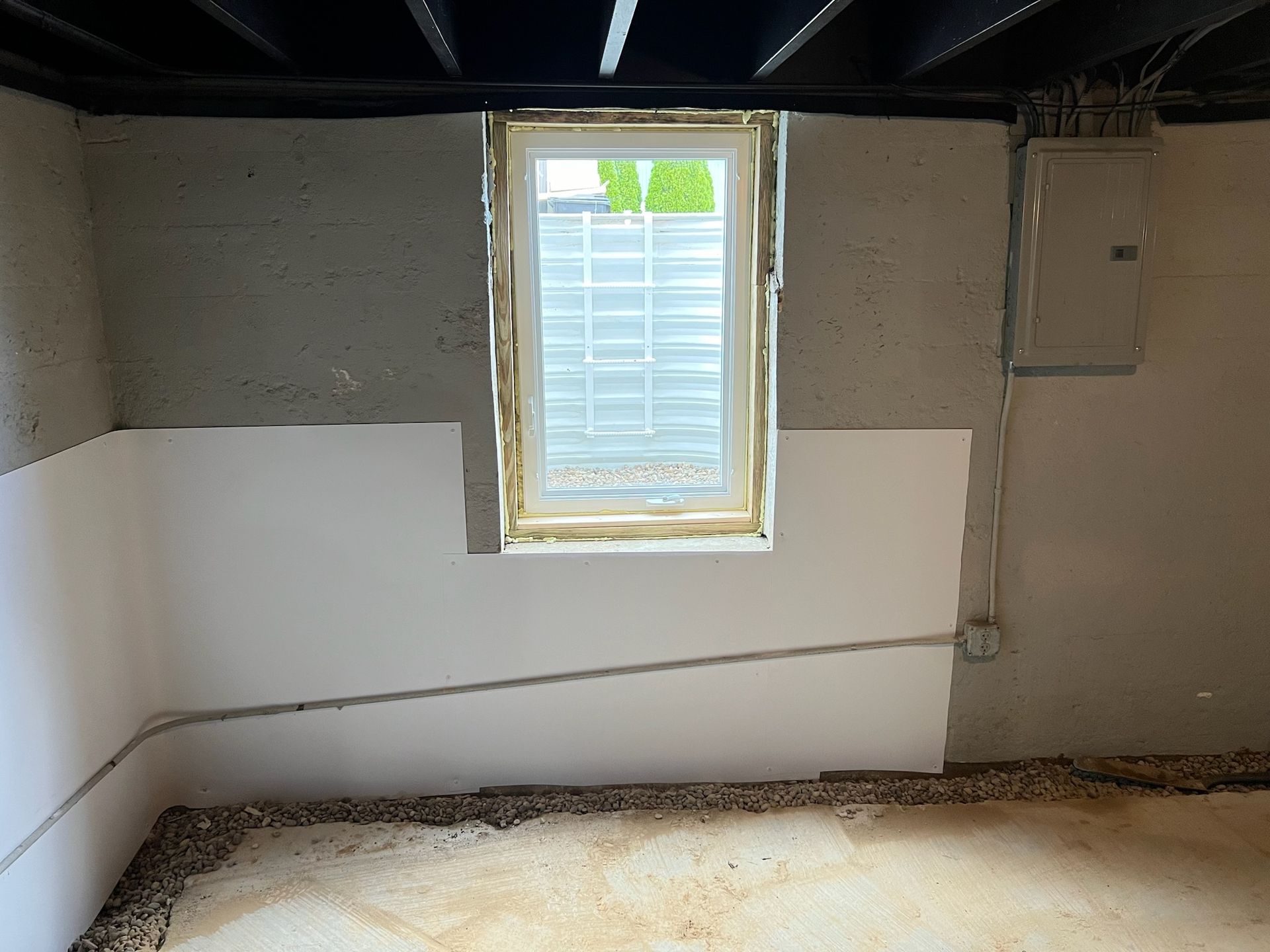 Basement interior with window, white panels, and electrical box on gray concrete wall.