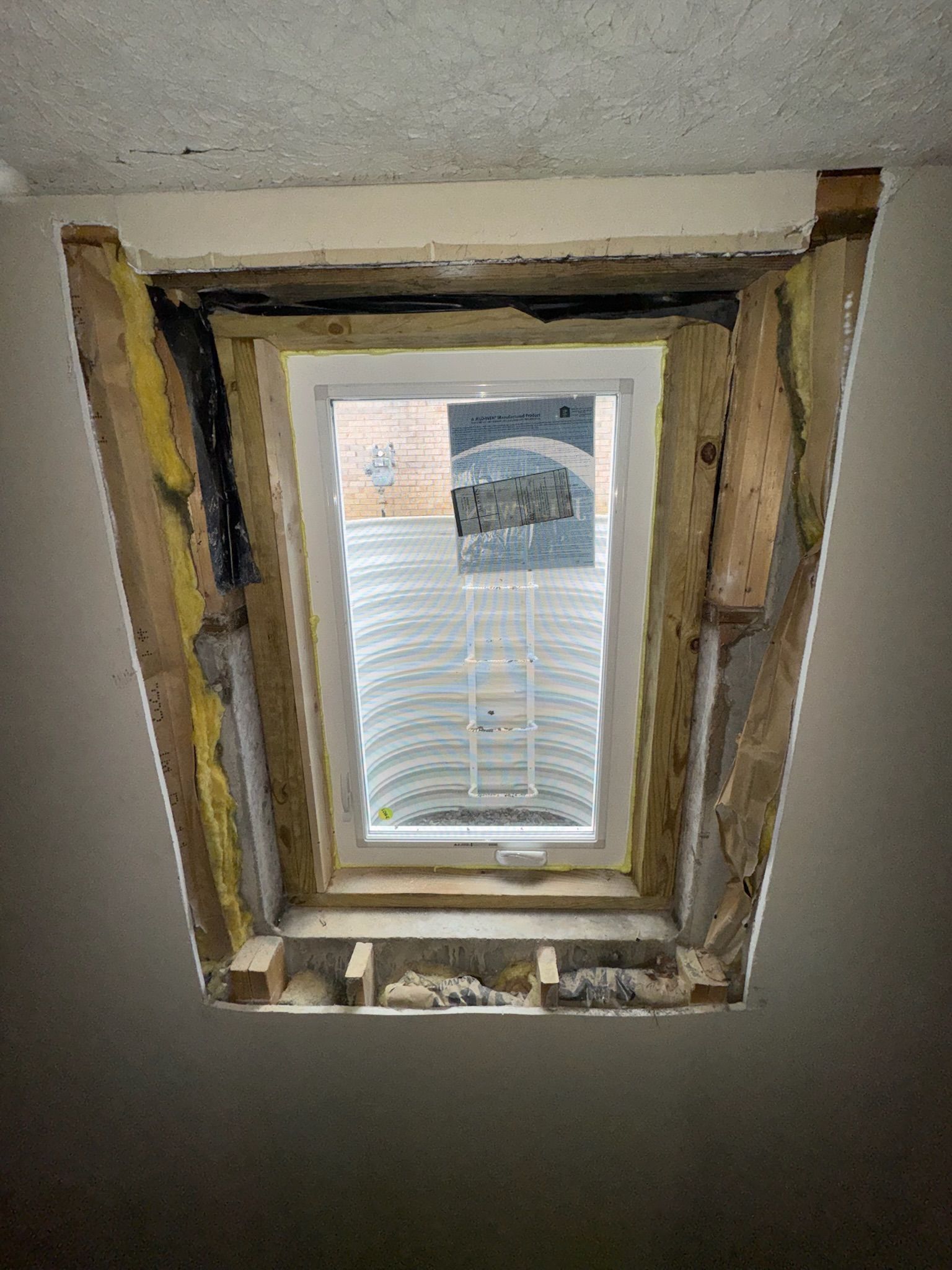 Window in a wall with exposed framing and insulation, looking into a window well.