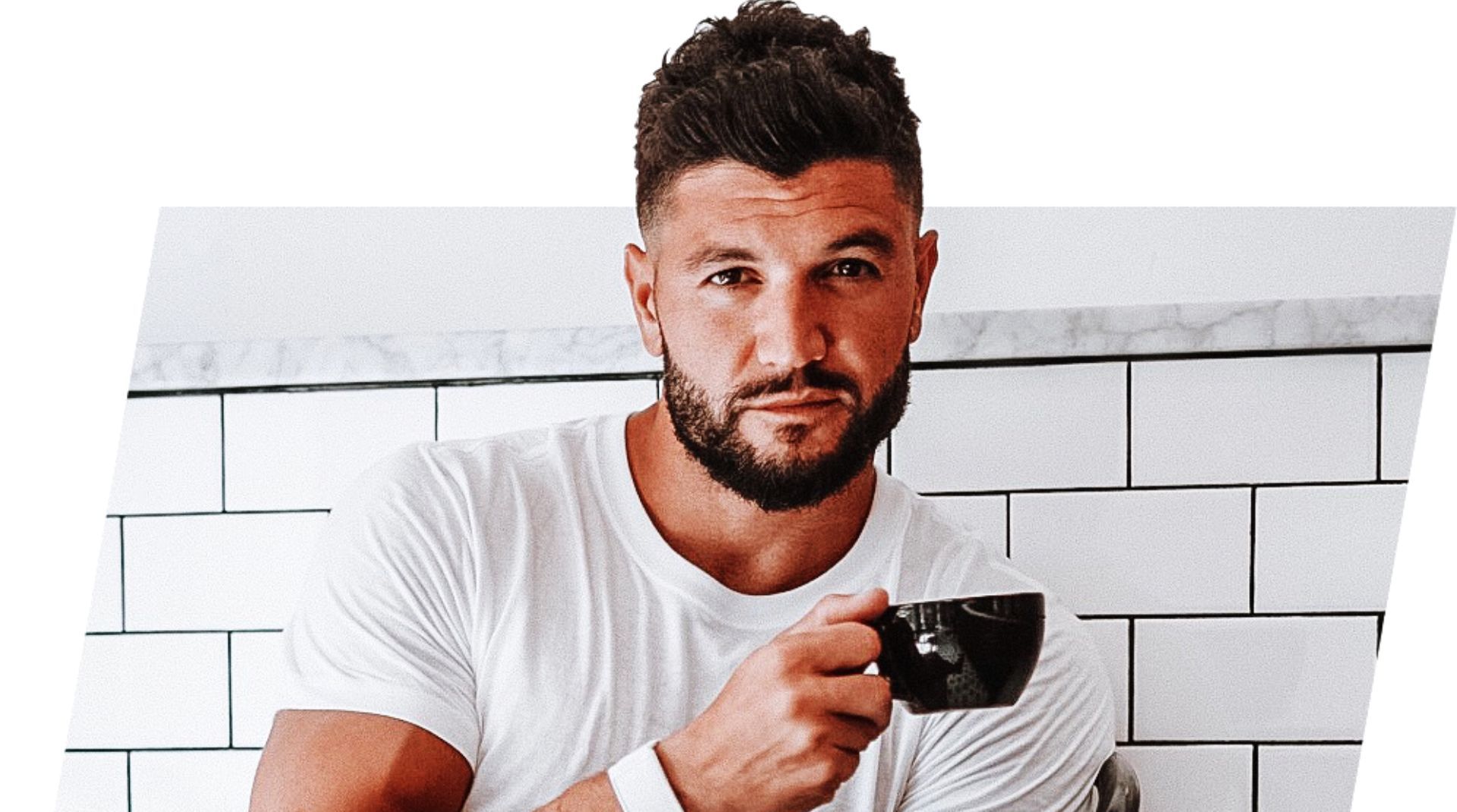 Brian Mazza holding a black coffee cup, wearing a white t-shirt, and looking confidently at the came