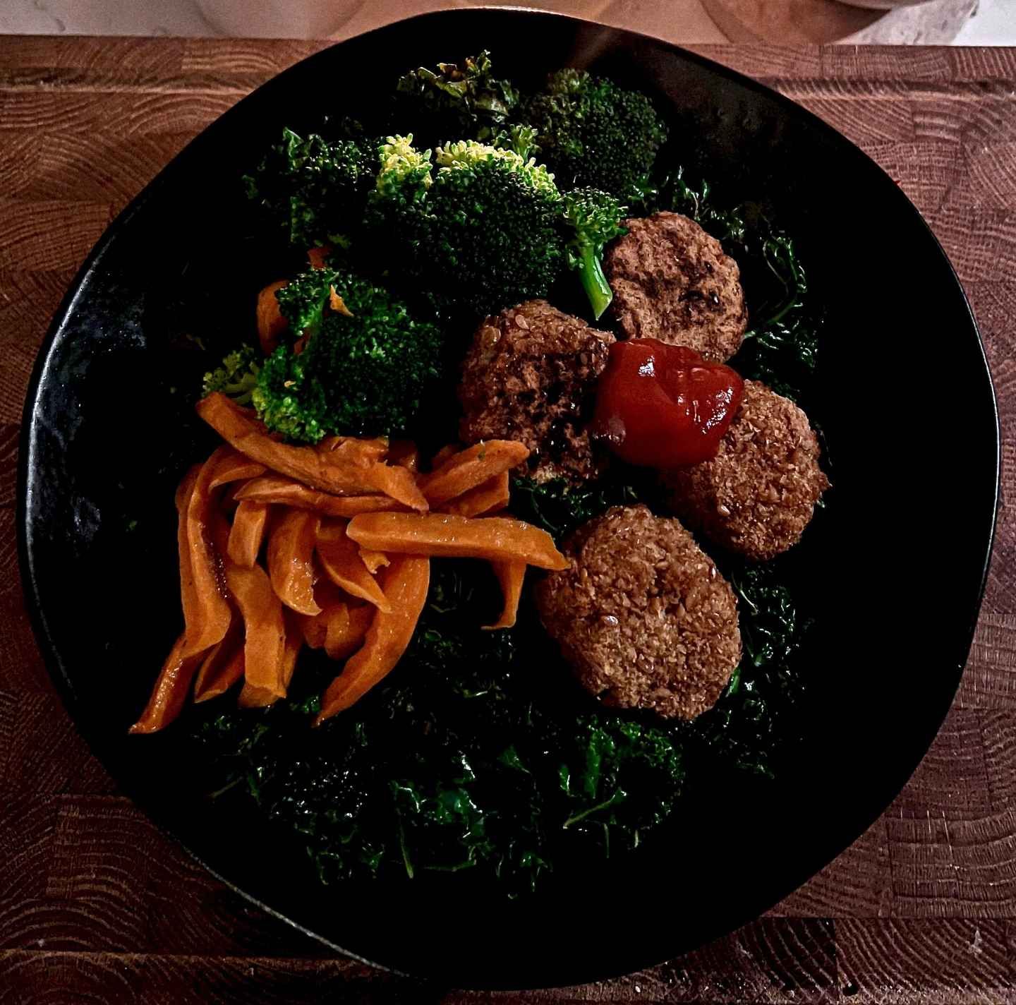 A black bowl filled with meatballs broccoli and sweet potatoes