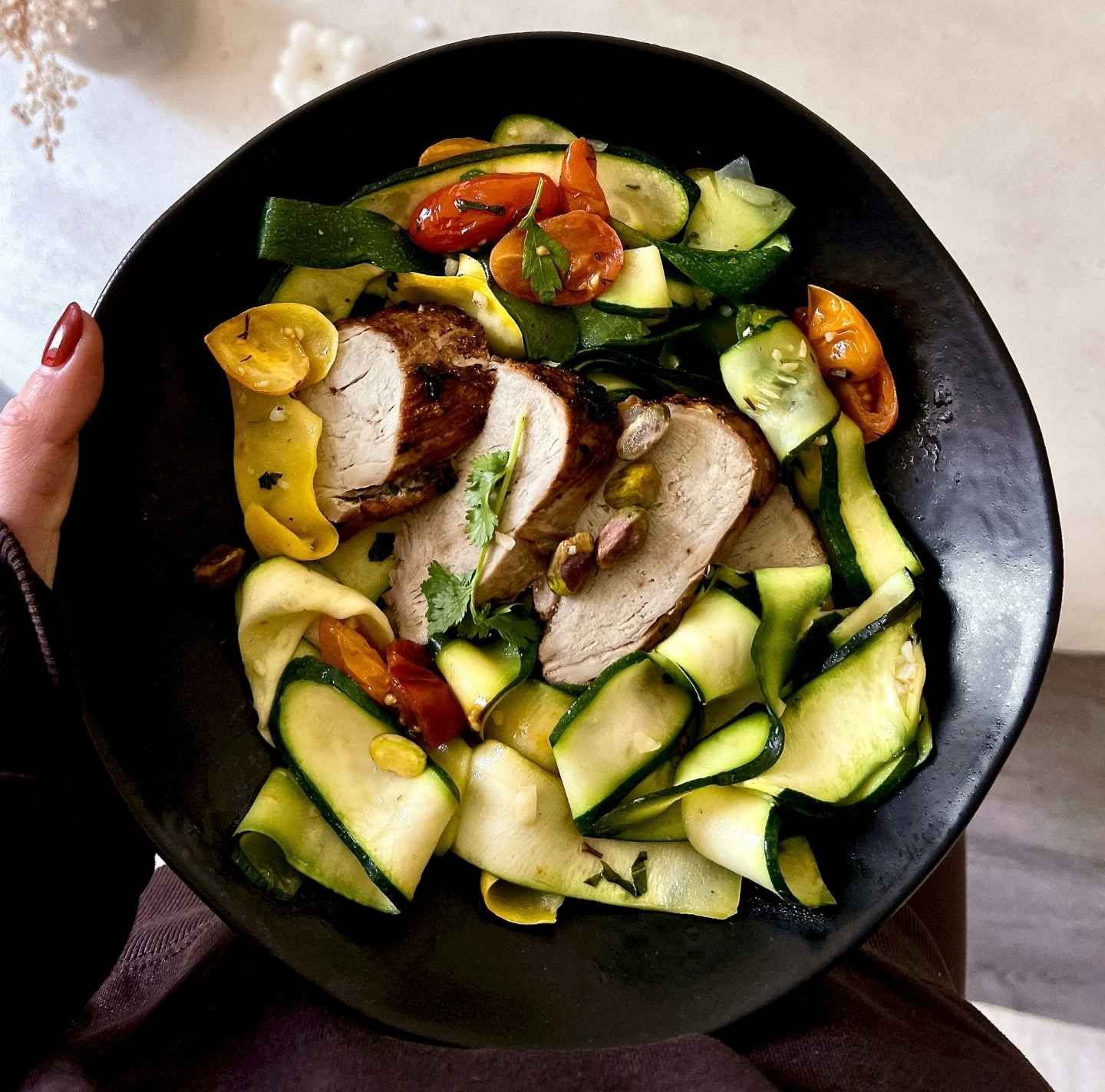 A person is holding a black plate of food with meat and vegetables.