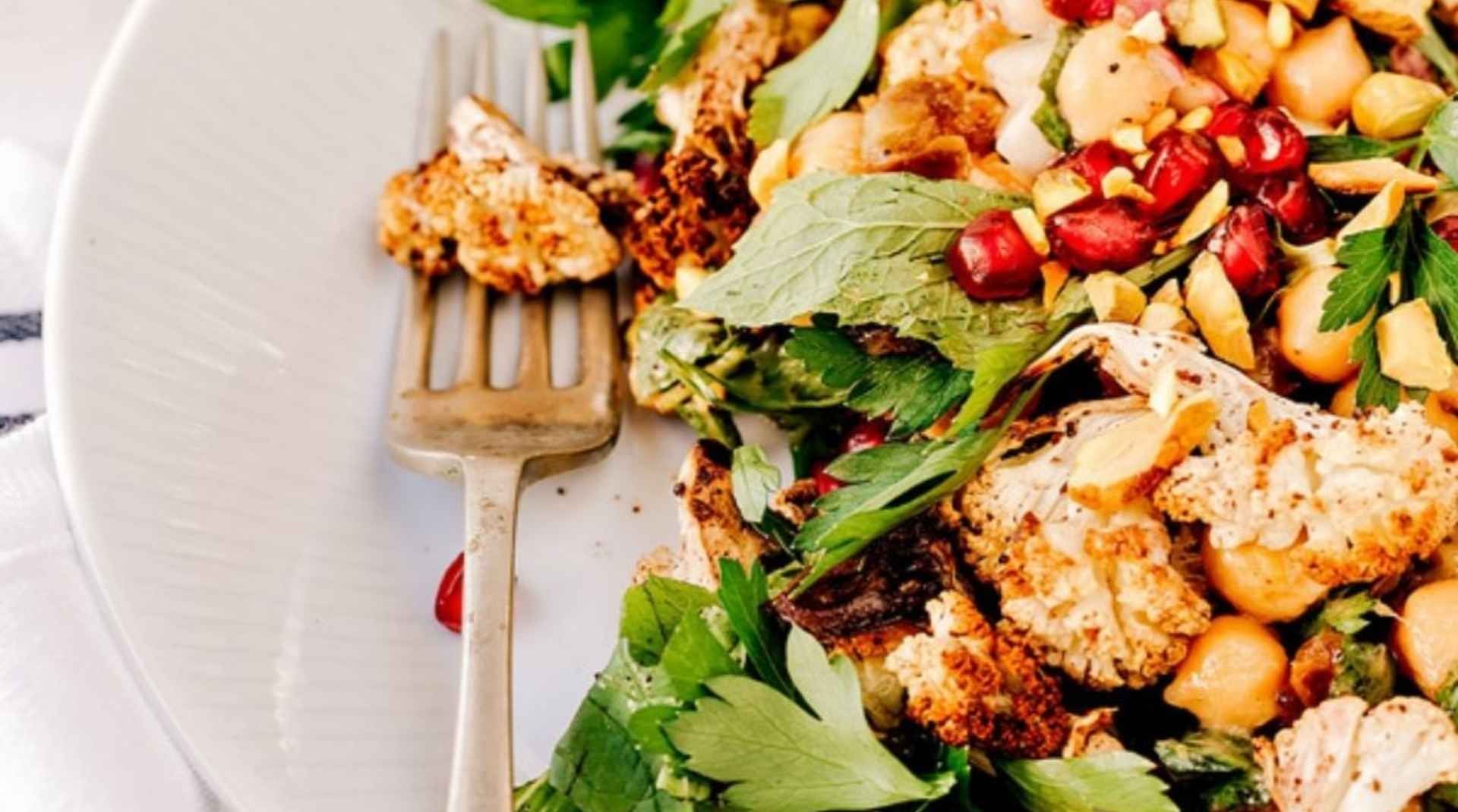 A vibrant roasted cauliflower salad with chickpeas, pomegranate seeds, fresh herbs, and nuts