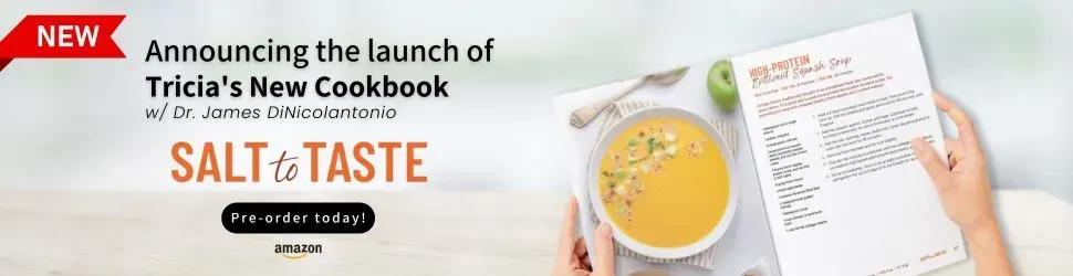 A person is holding a cookbook next to a bowl of soup.