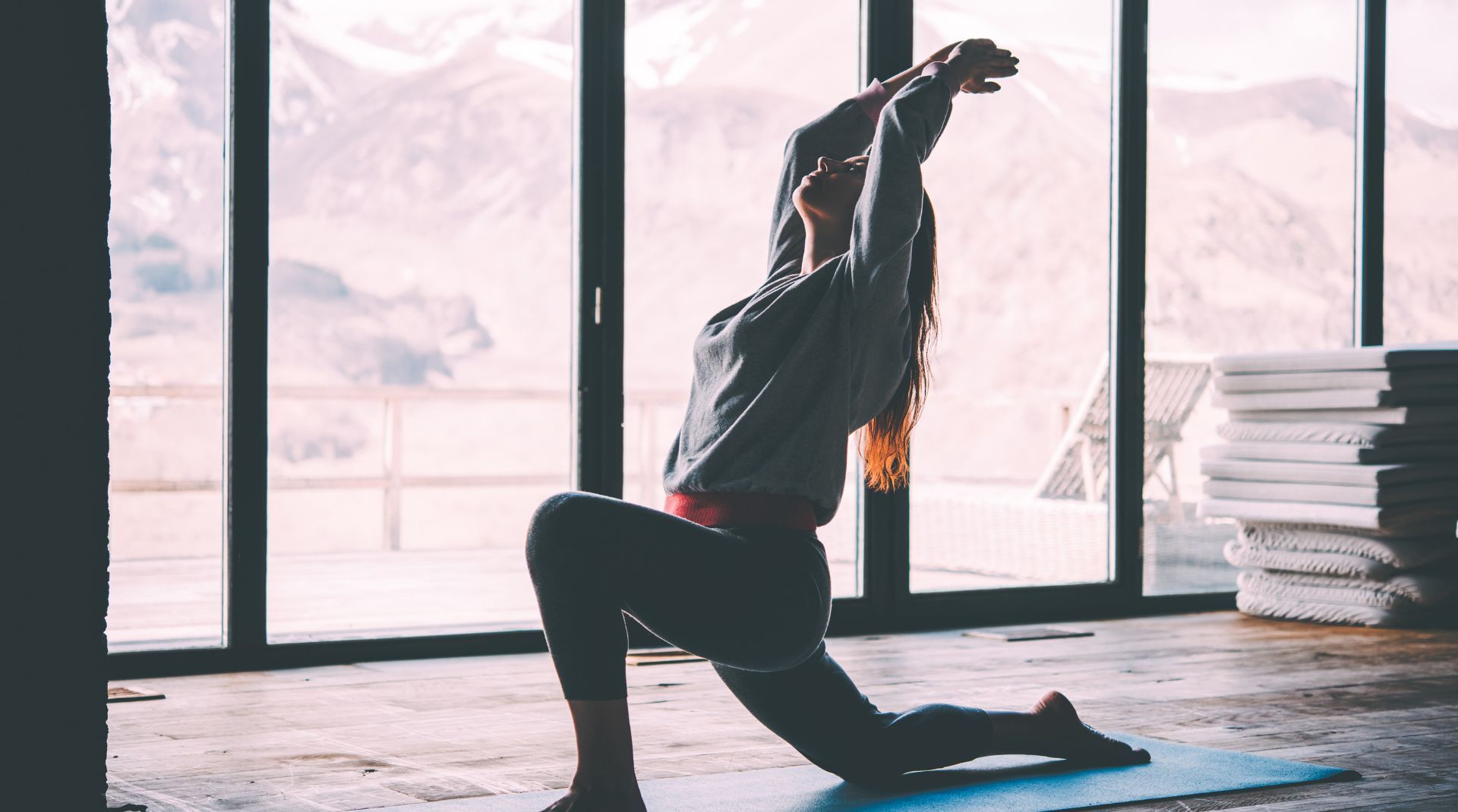 A woman practicing yoga indoors with a scenic mountain view, stretching in a deep lunge pose