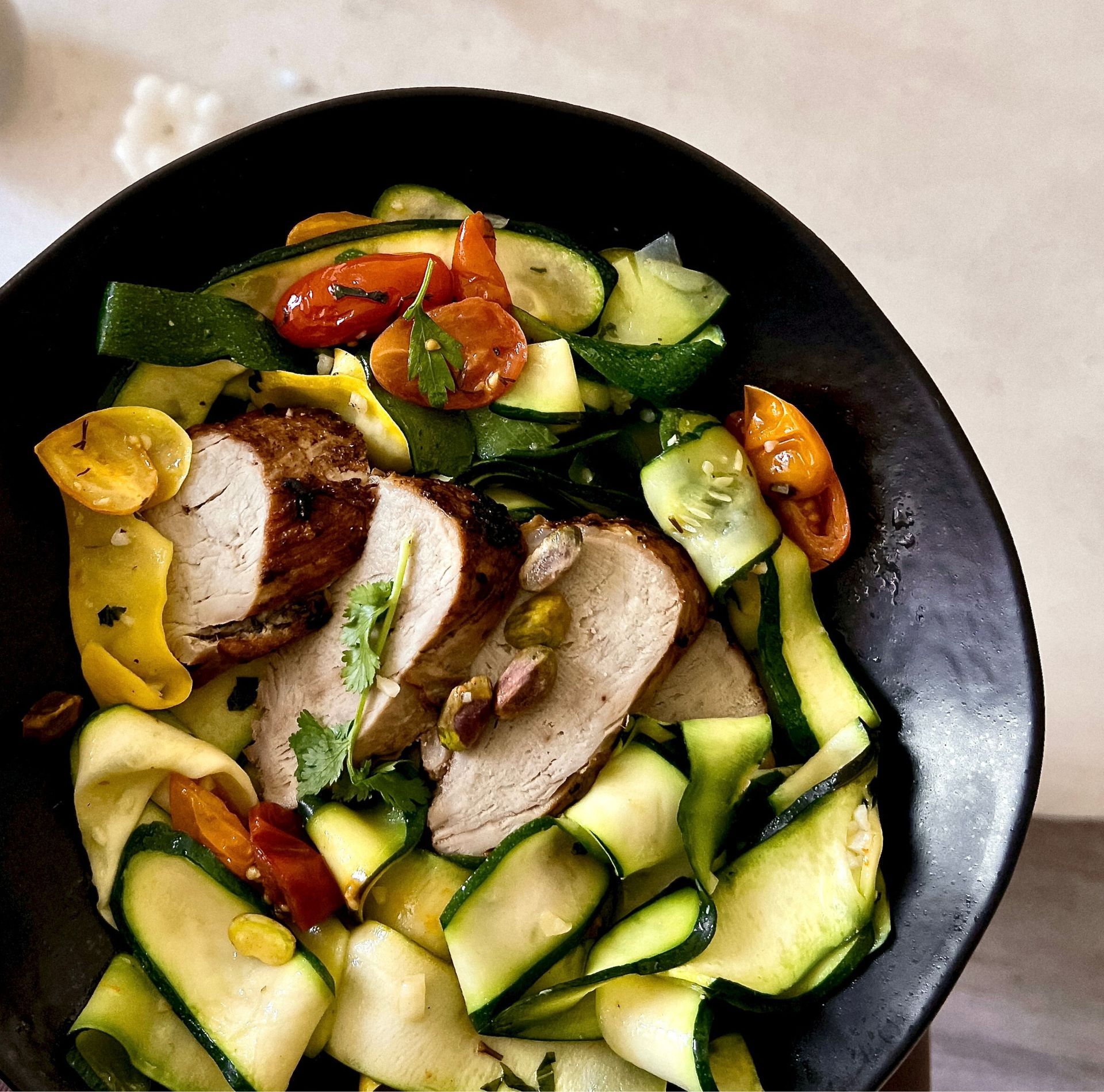 High-protein, nutrient-dense meal from The Program by Daily Dose, featuring sliced roasted chicken with pistachios, zucchini ribbons, blistered cherry tomatoes, and fresh herbs for optimal performance and recovery.