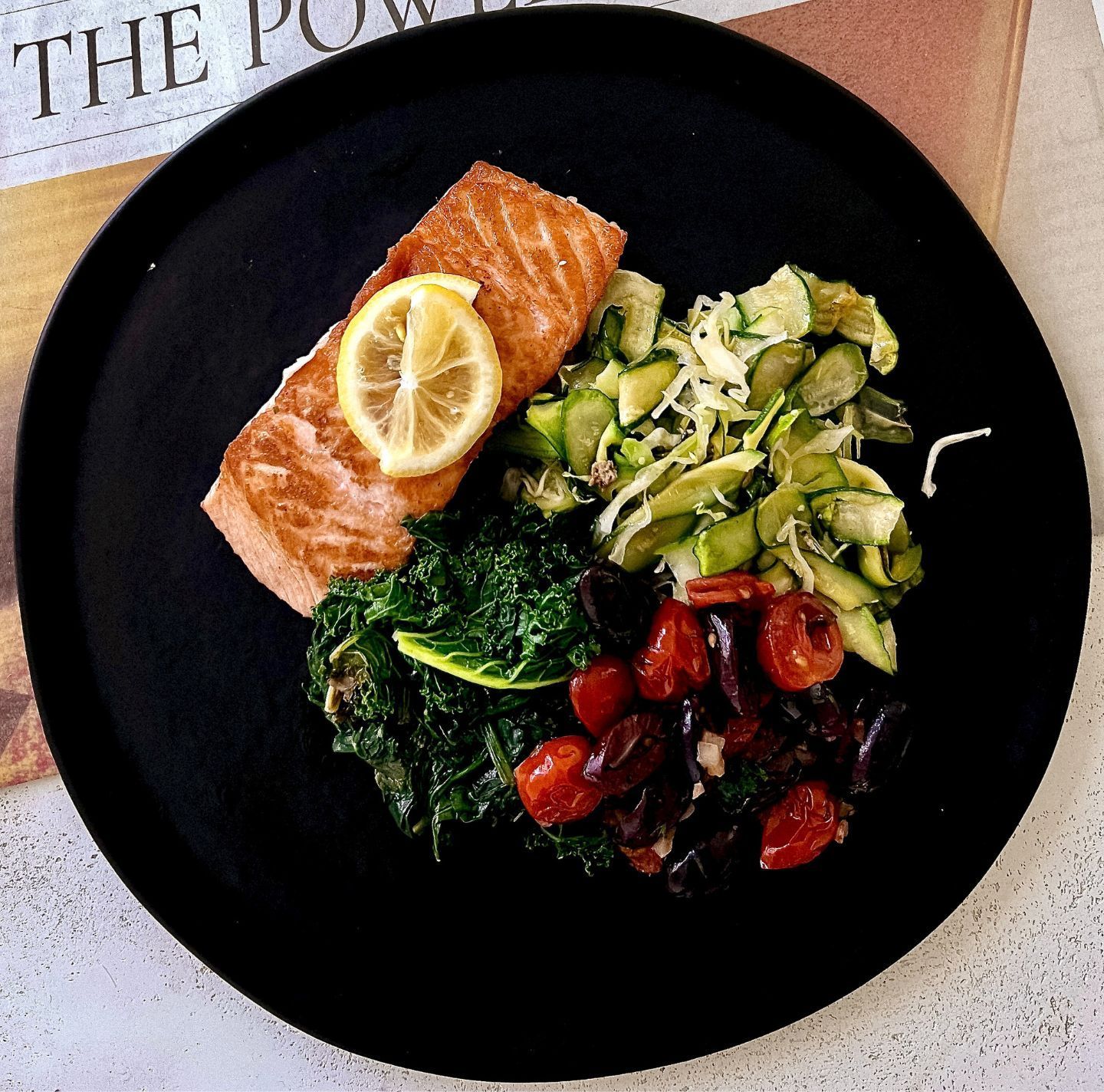 A black plate with a piece of salmon and vegetables on it