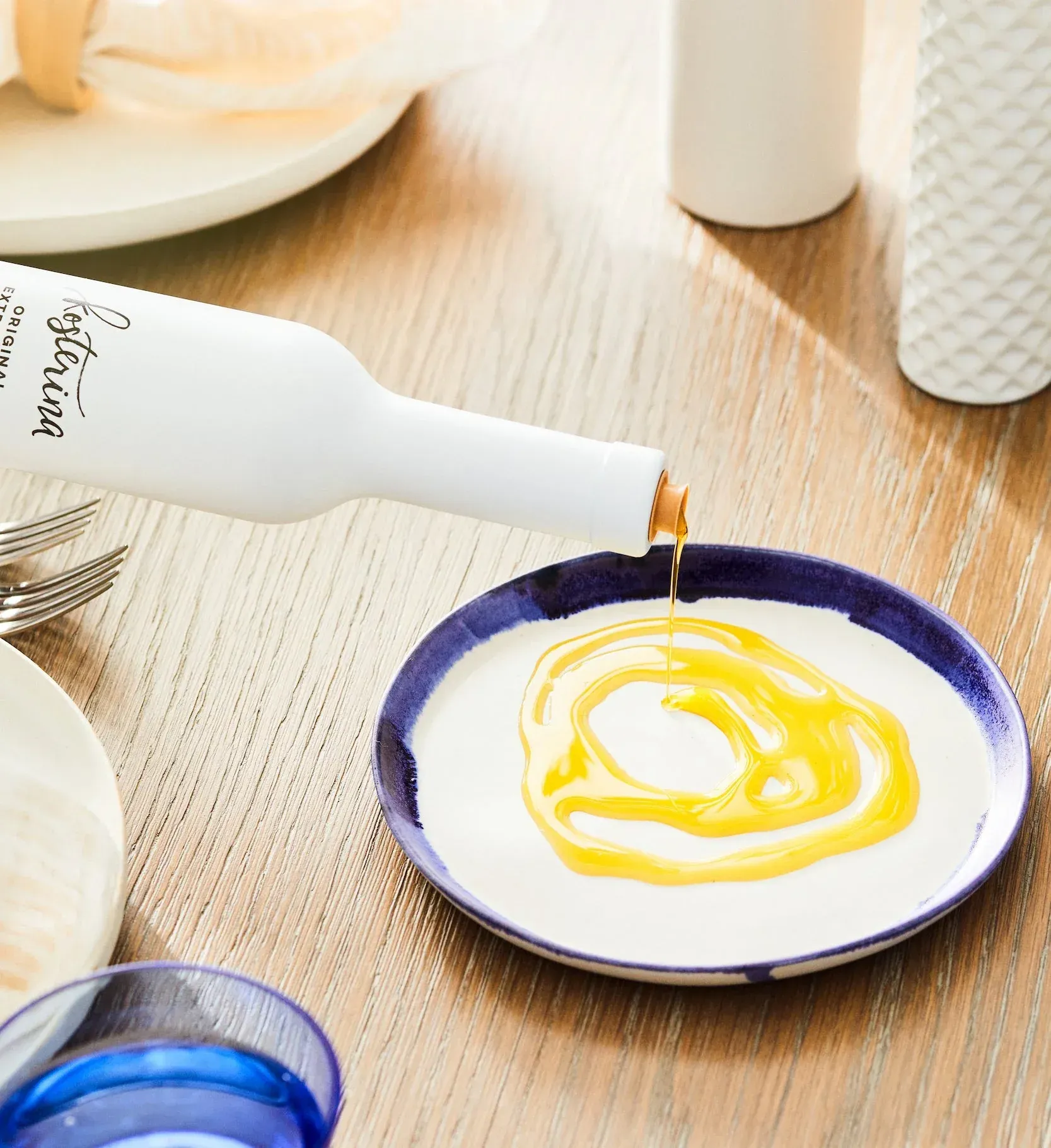 Golden extra virgin olive oil being poured from a white Kosterina bottle onto a ceramic plate