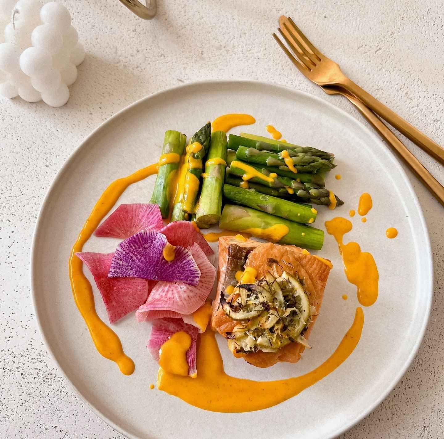 Paleo meal by Tricia Williams for Daily Dose featuring herb-crusted salmon with lemon, roasted asparagus, and vibrant watermelon radish, drizzled with a turmeric-infused sauce. A chef-crafted, nutrient-dense dinner designed for optimal health and longevity.