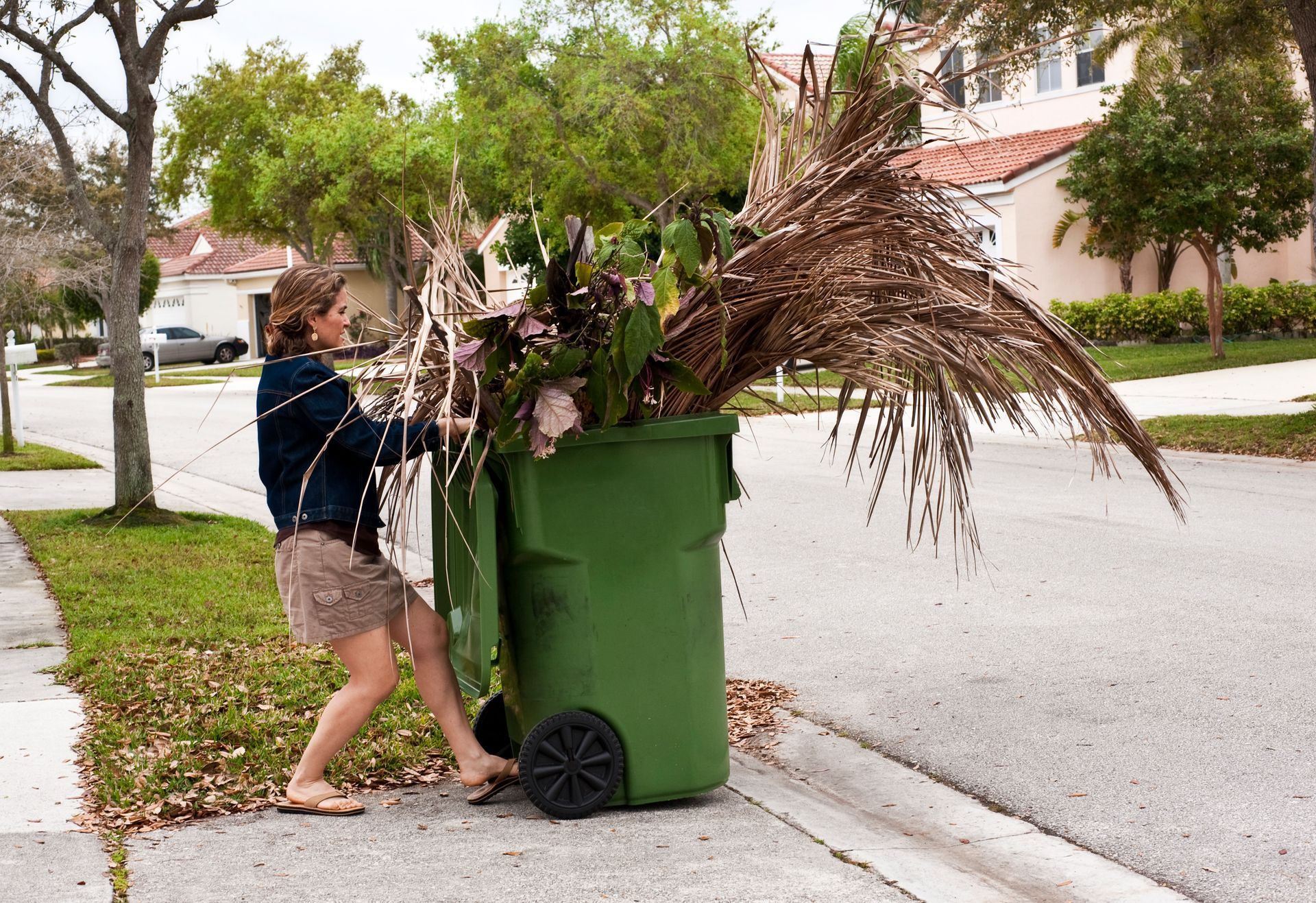 A woman is pushing a green trash can full of branches