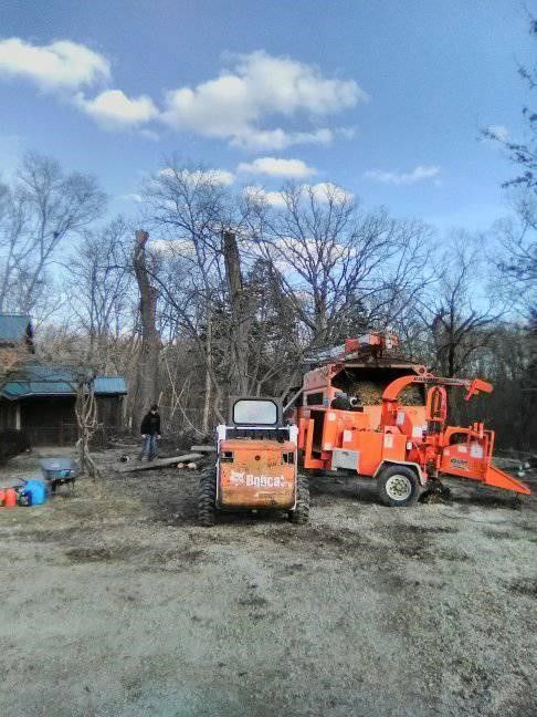 A tractor and a tree chipper are parked in a dirt lot.