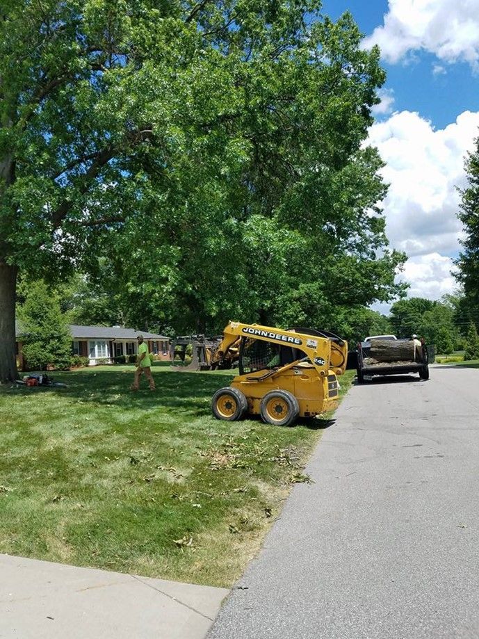 A yellow lawn mower is parked on the side of the road next to a truck.