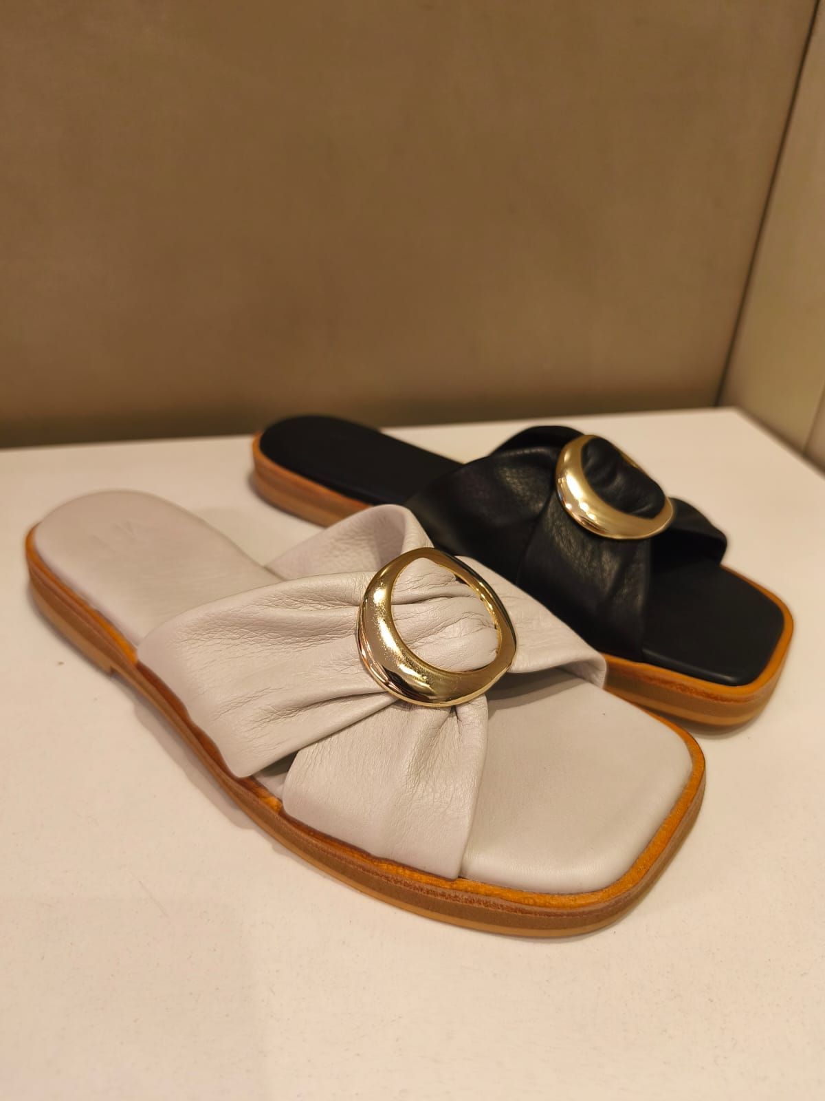 Dos sandalias: una blanca y otra negra, cada una con una hebilla dorada y punta cuadrada