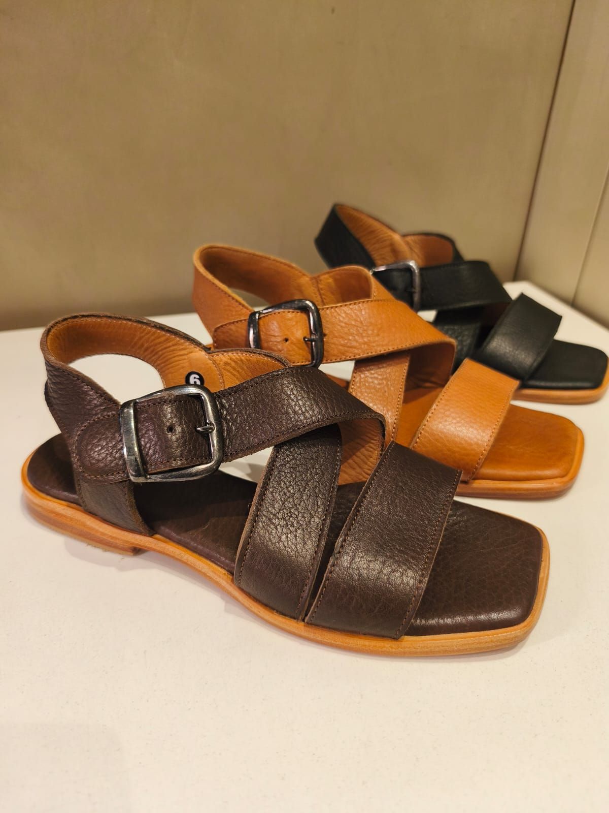 Tres sandalias de cuero en color marrón, tostado y negro, con punta cuadrada y tiras en el tobillo.