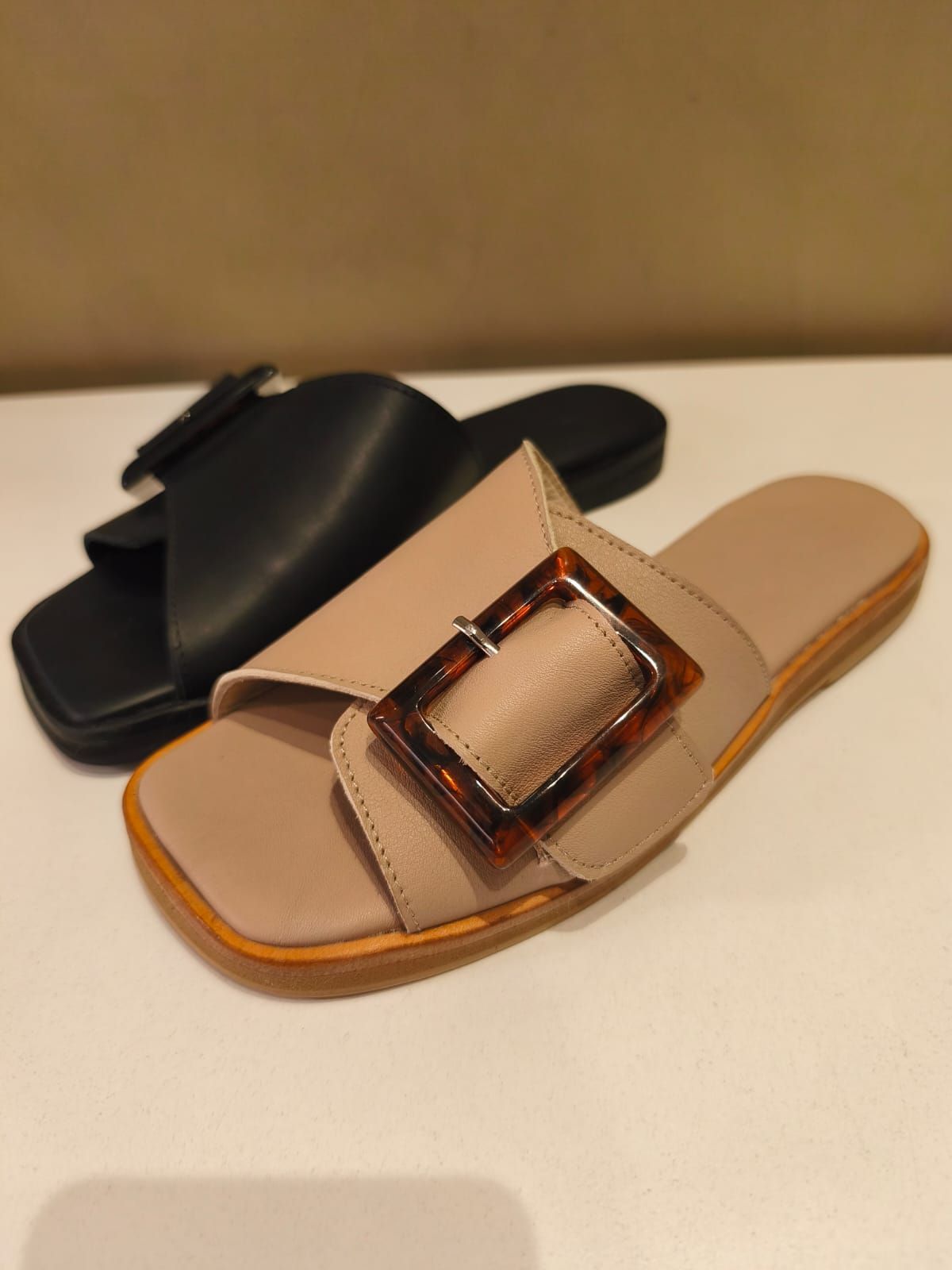 Dos sandalias: una de piel color canela con hebilla de carey marrón en la parte delantera, y otra de piel negra