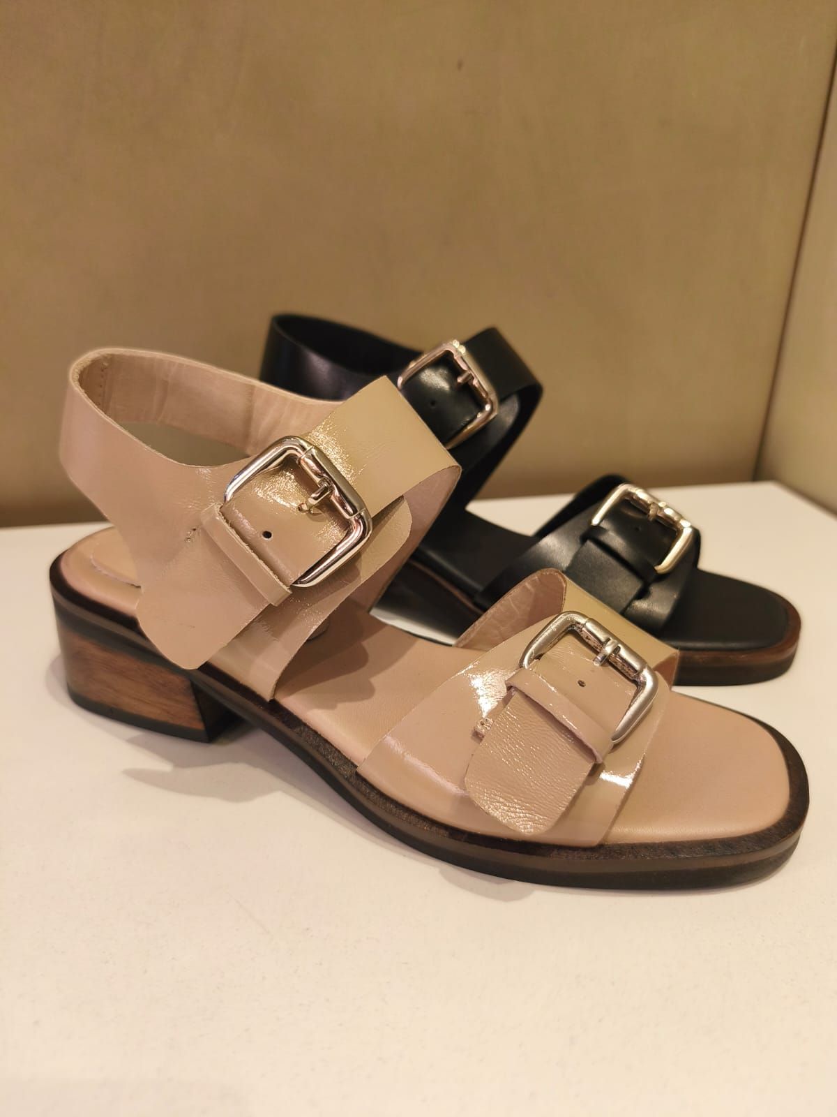 Sandalias beige y negras con detalles de hebillas sobre superficie blanca.