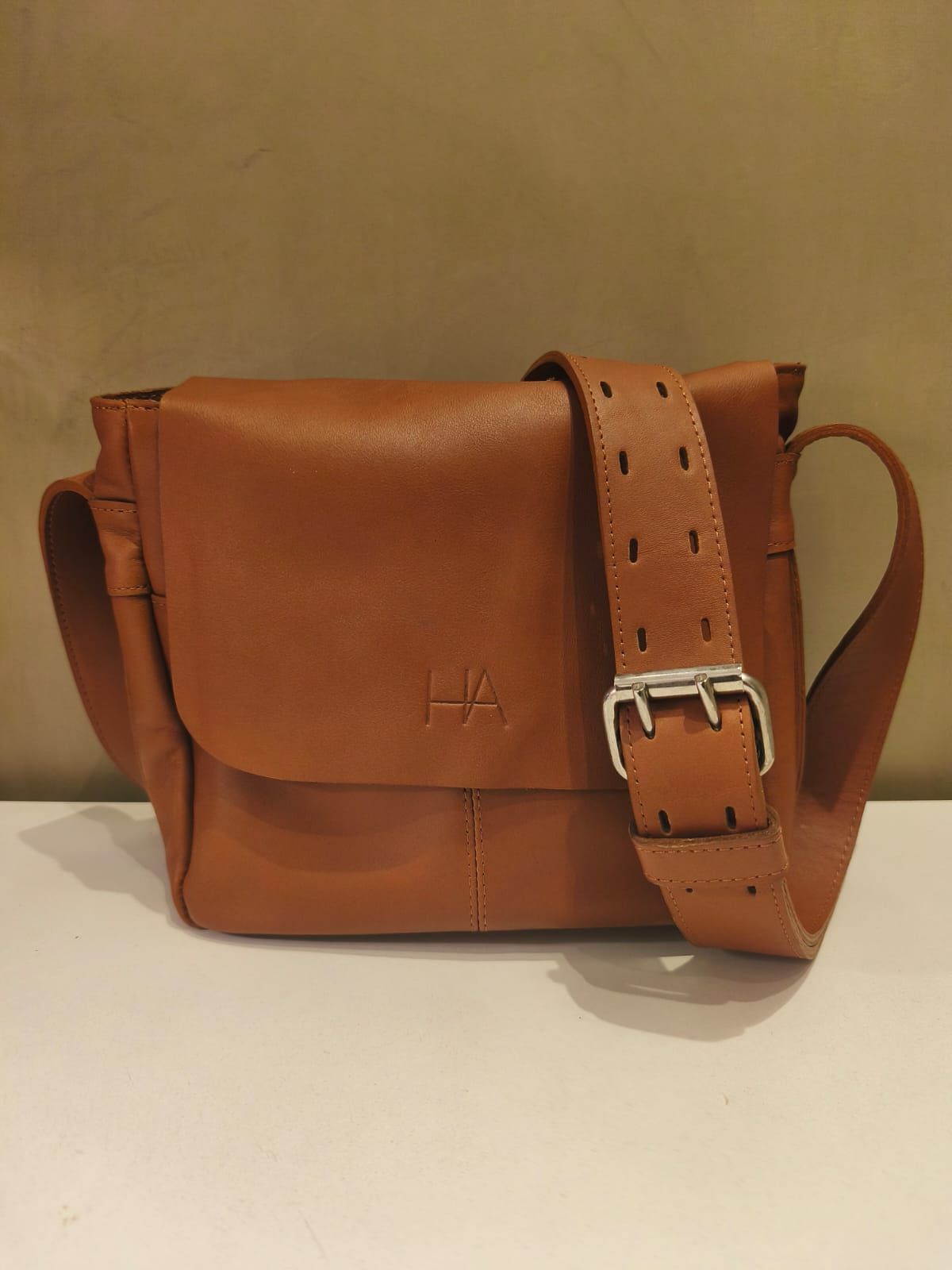 Bolso bandolera de piel marrón con hebilla plateada y correa perforada.