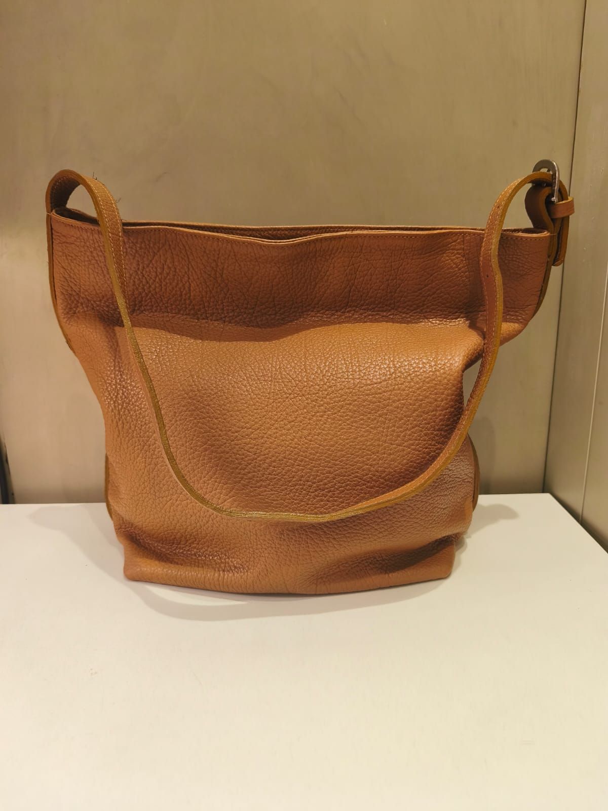 Bolso de hombro de piel marrón sobre estante blanco.