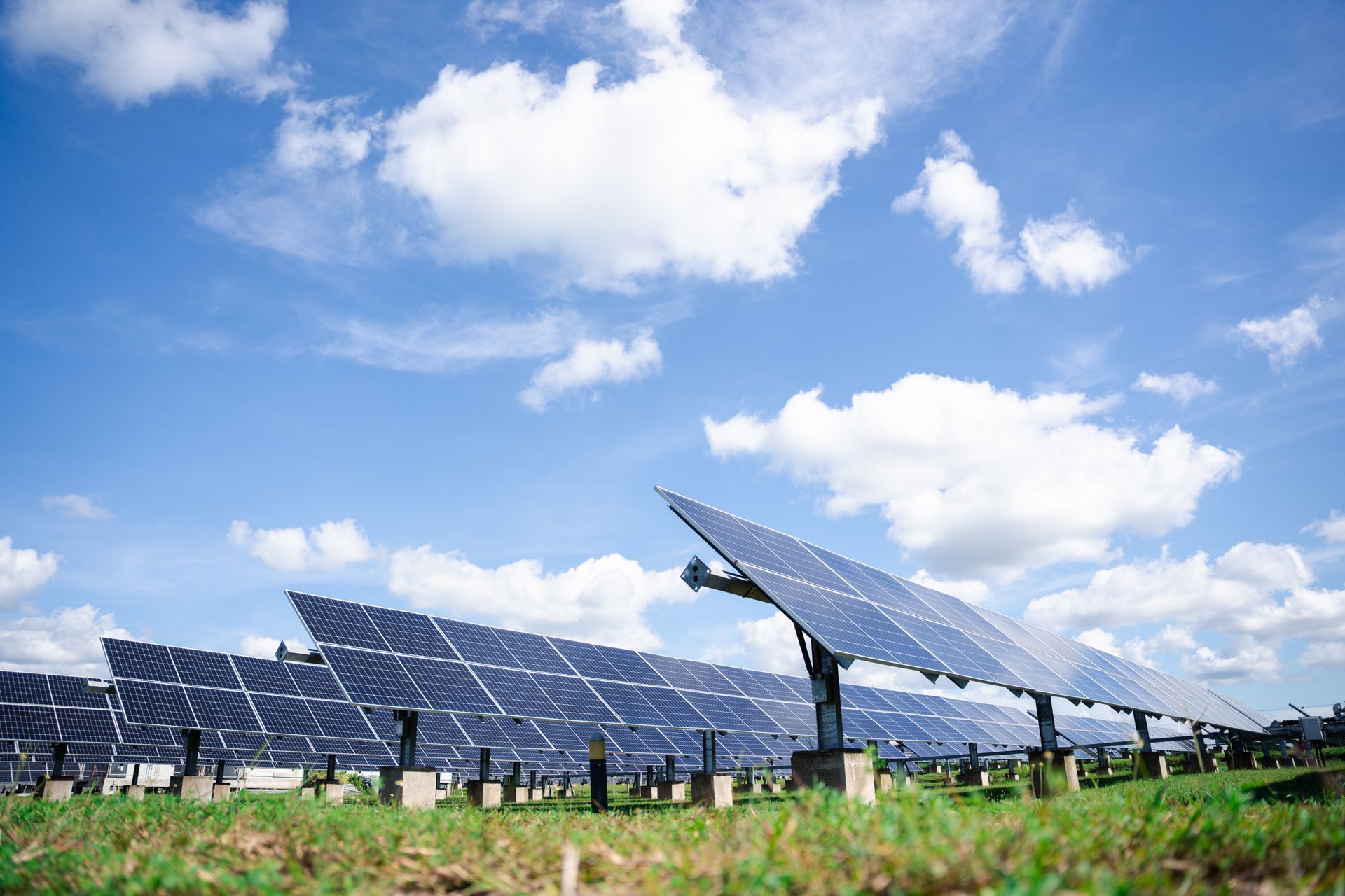 Solar panels in a field against a bright blue sky with fluffy white clouds.