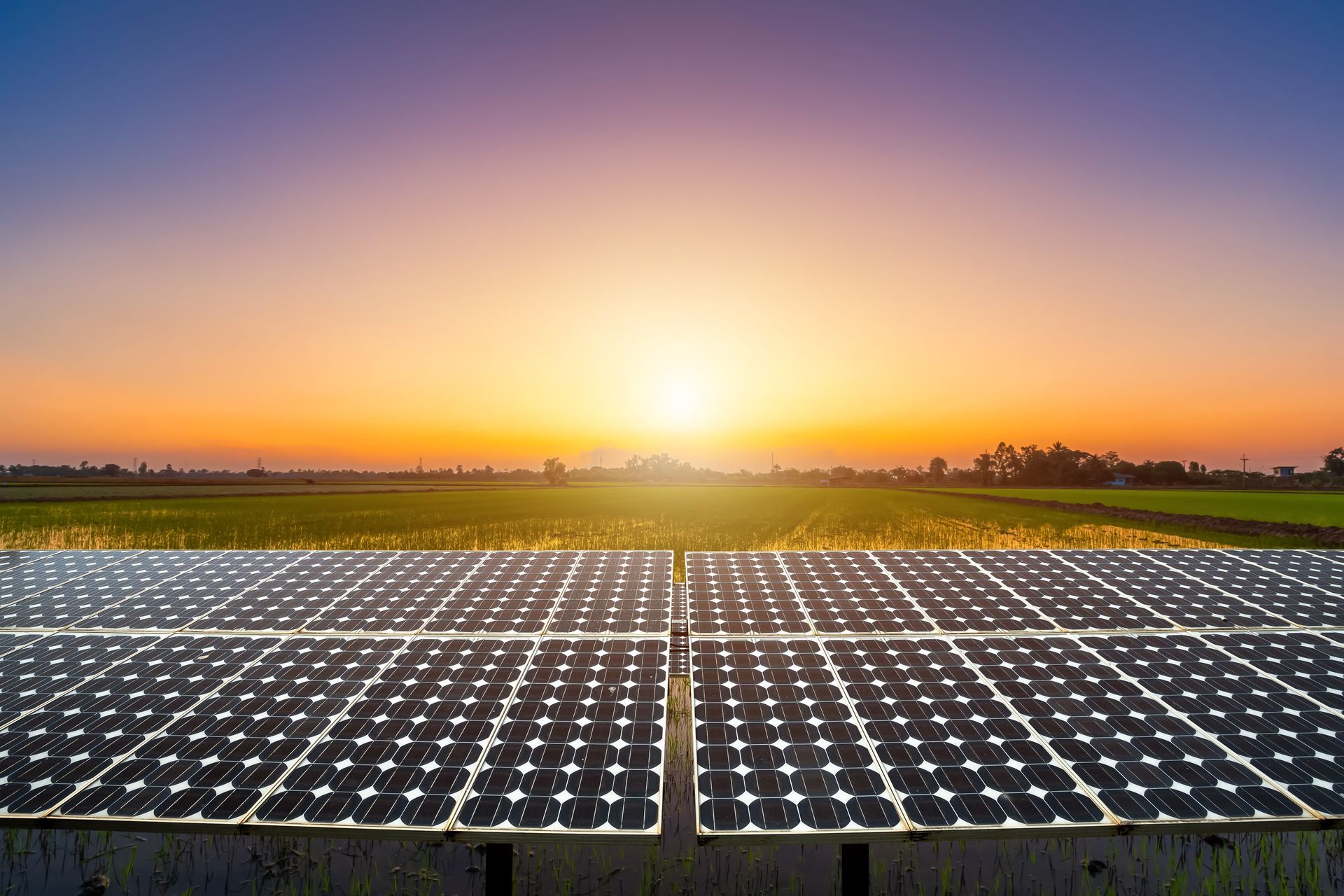 Solar panels in a field at sunset with a vibrant orange and blue sky.