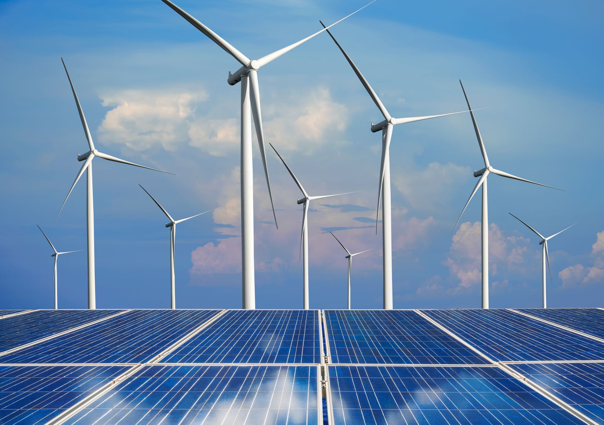 Solar panels and wind turbines in a field under a bright blue sky.