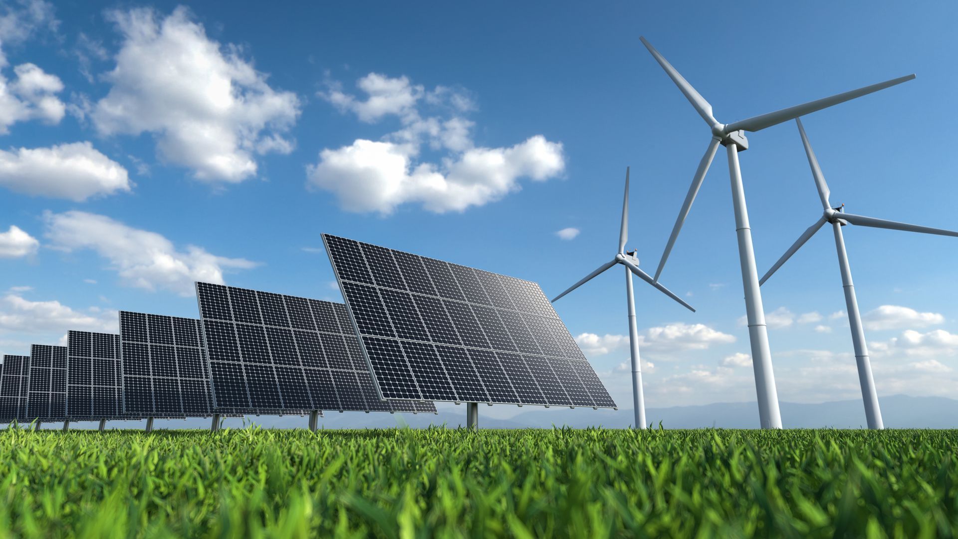 Solar panels and wind turbines in a grassy field under a blue sky with clouds.