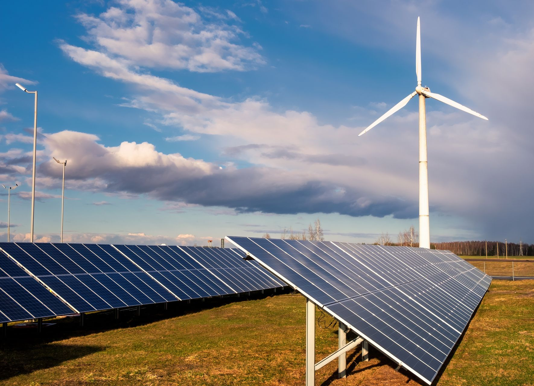 Solar panels and wind turbine generating renewable energy outdoors under a cloudy sky.