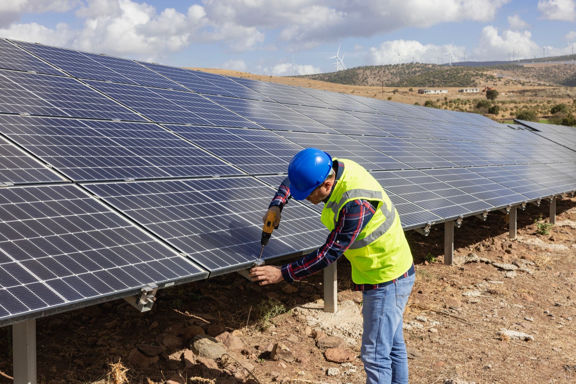 Worker installing solar panels in a field, wearing a hard hat and safety vest.