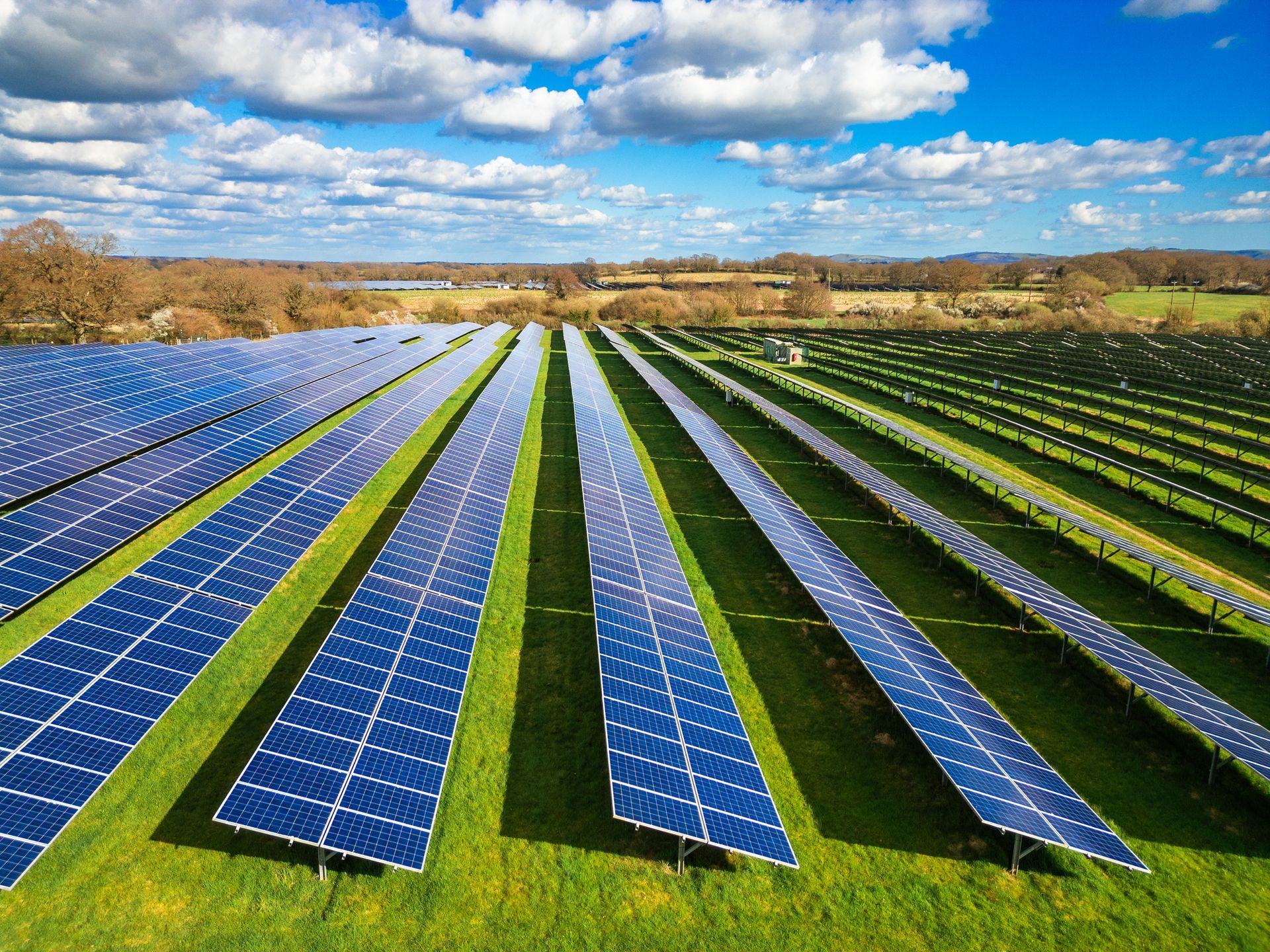 Solar panels arranged in rows on a grassy field under a blue sky with clouds.
