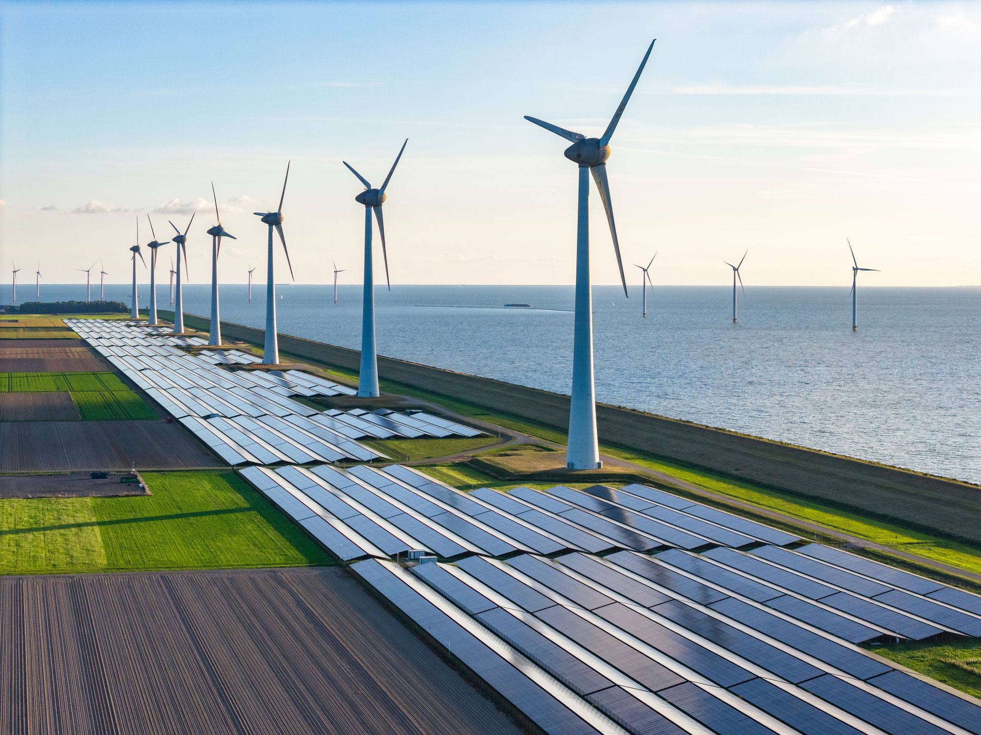 Solar panels and wind turbines on a coastal landscape, blue sky, generating renewable energy.