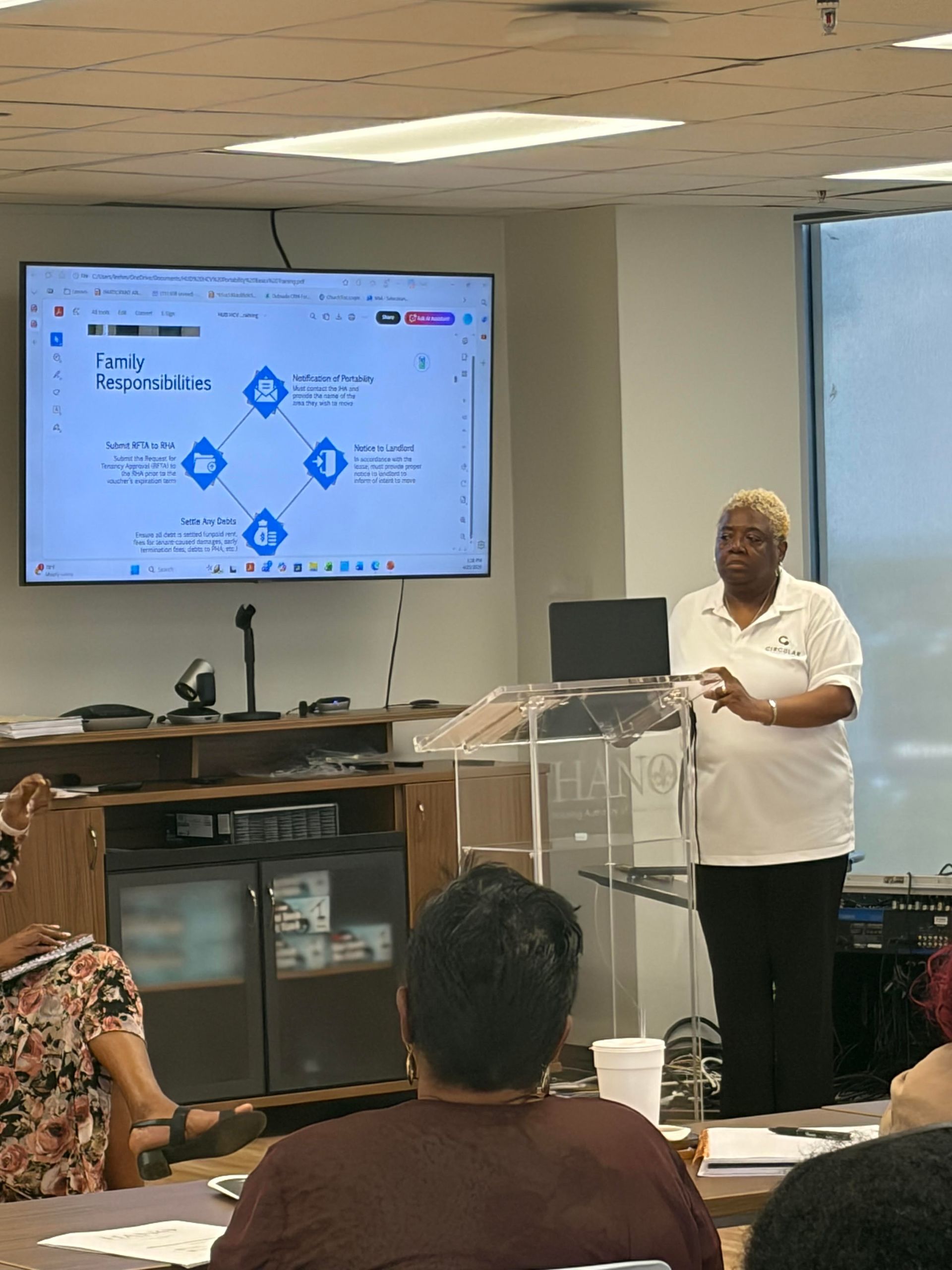 A group of people are sitting at tables in front of a projector screen.