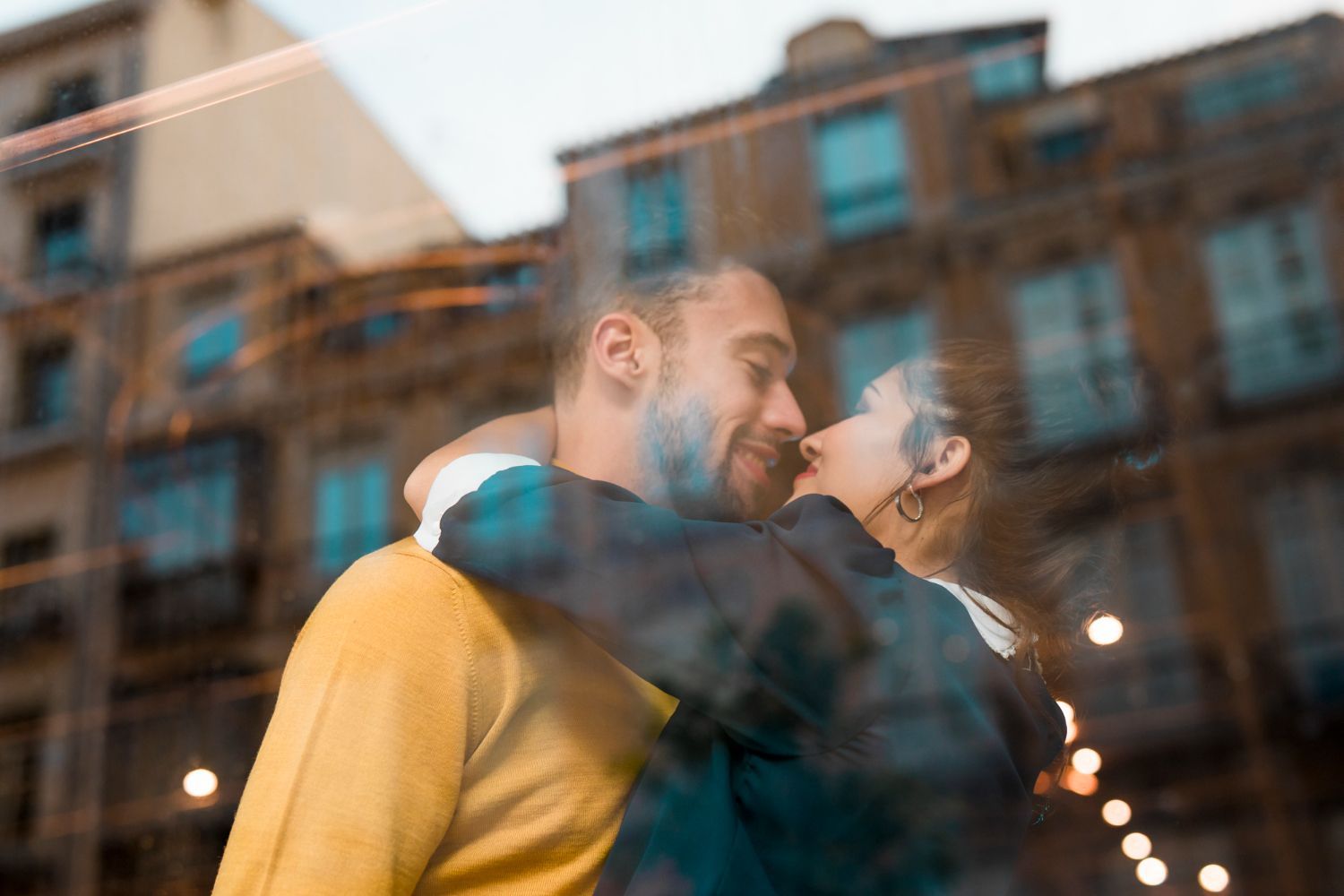A man and a woman are kissing in front of a window.