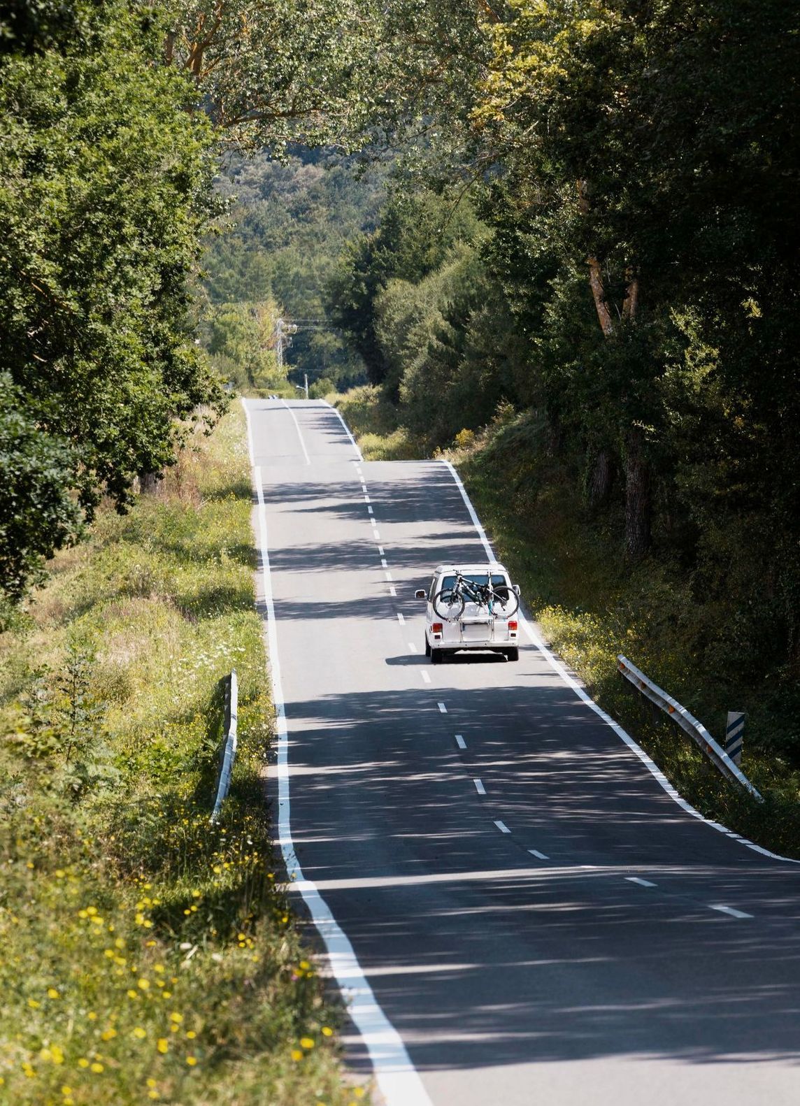 A white car is driving down a country road surrounded by trees.