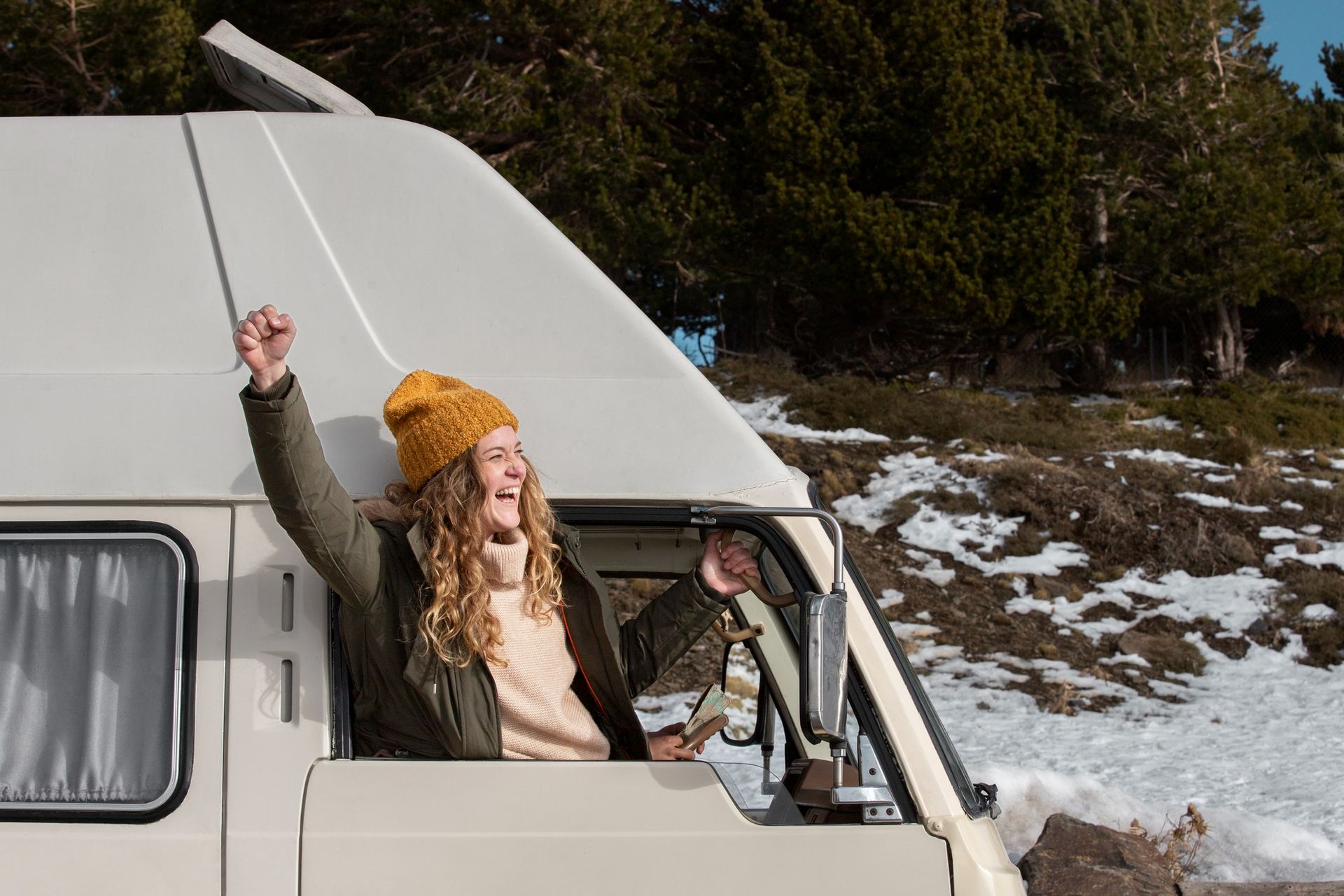 A woman is sitting in a van with her arms in the air.