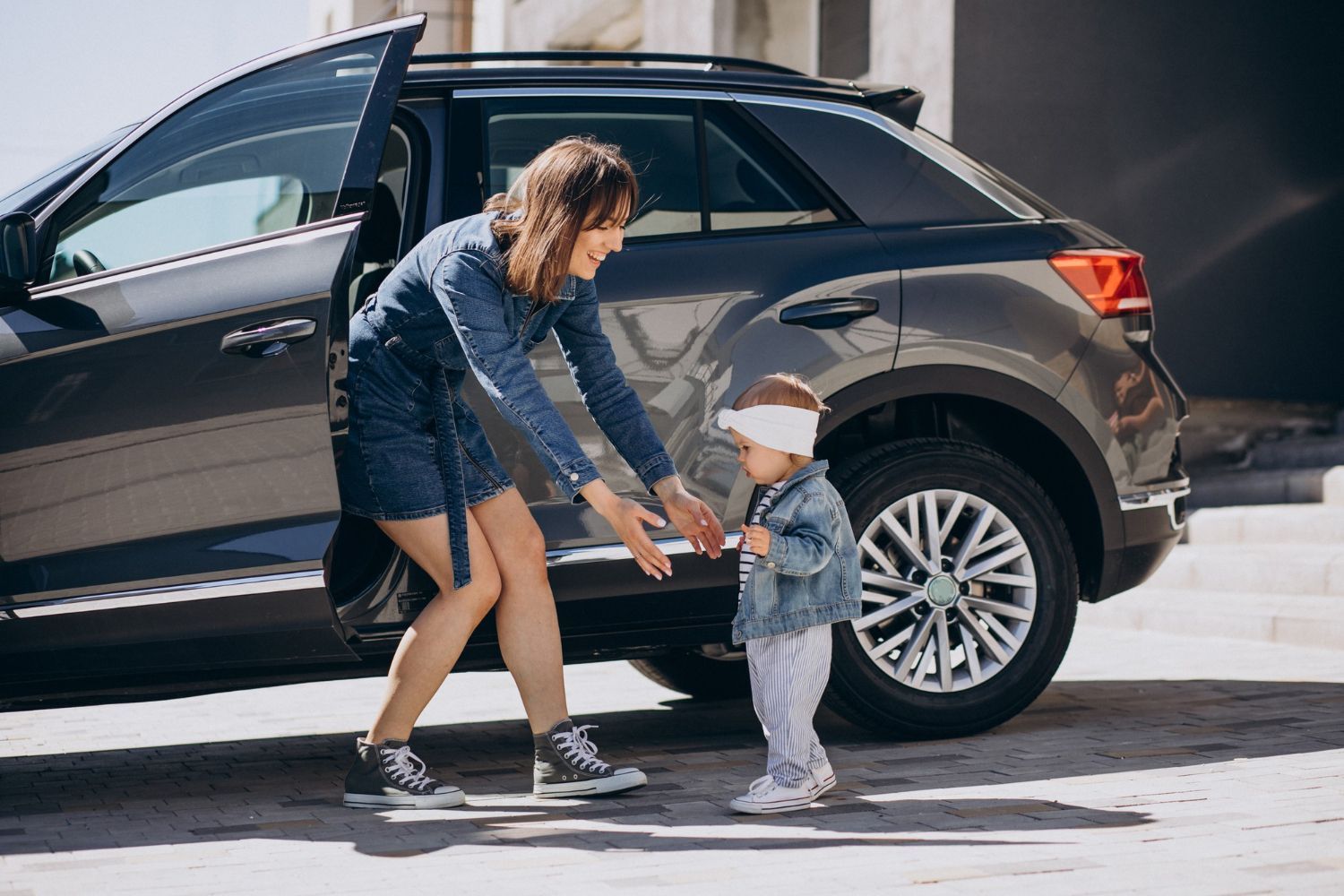 A woman is helping a little girl get out of a car.