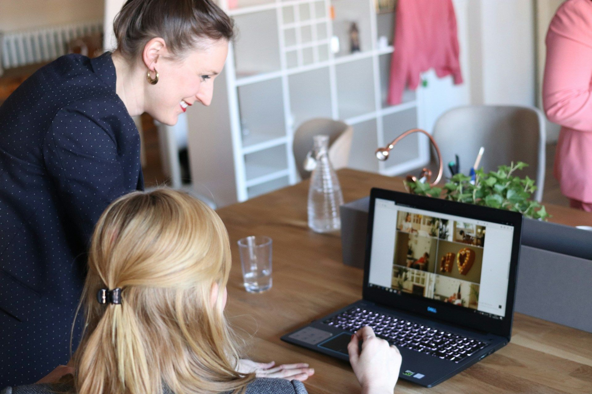 Two women are looking at a laptop computer on a wooden table.