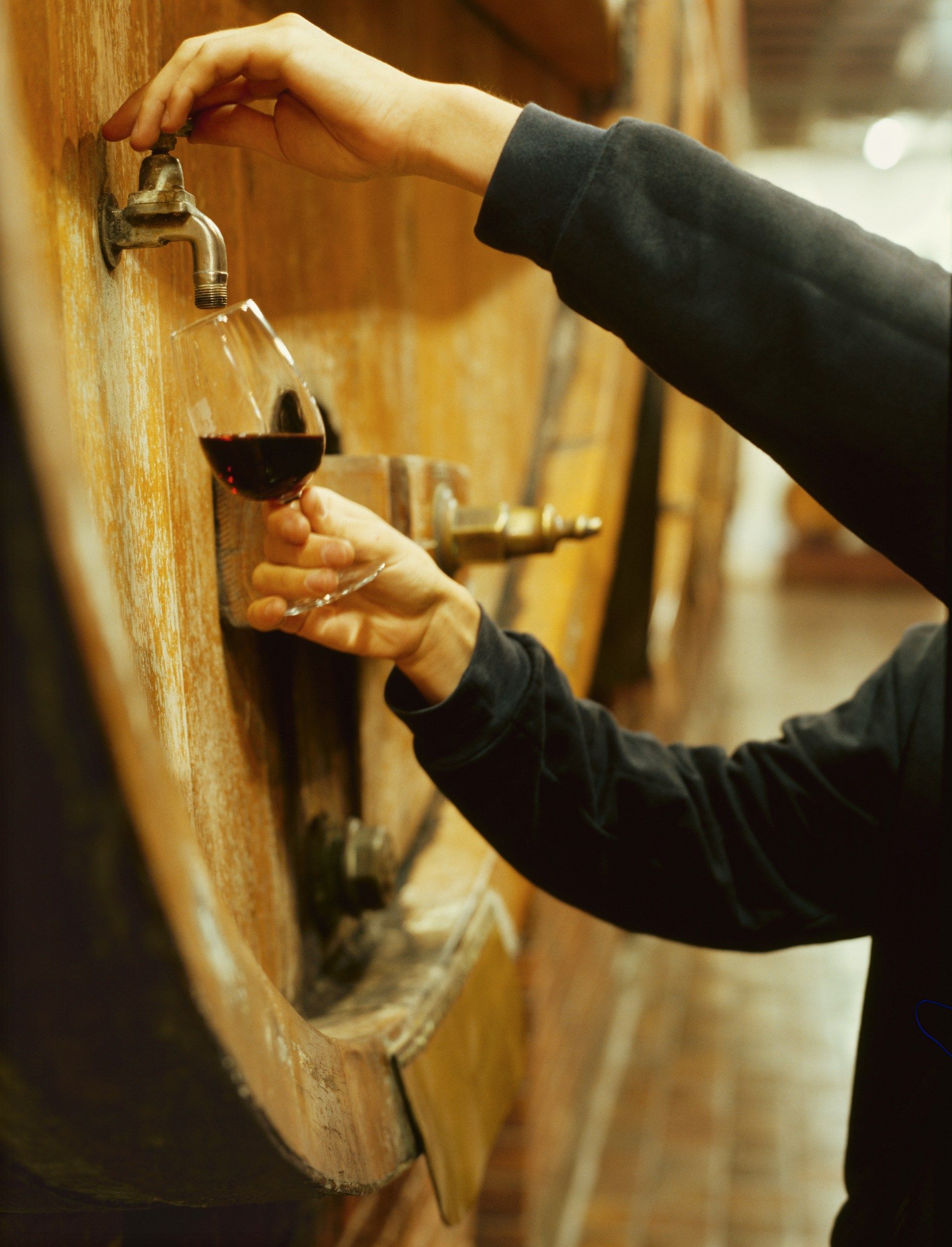 A person pouring a glass of wine into a wooden barrel