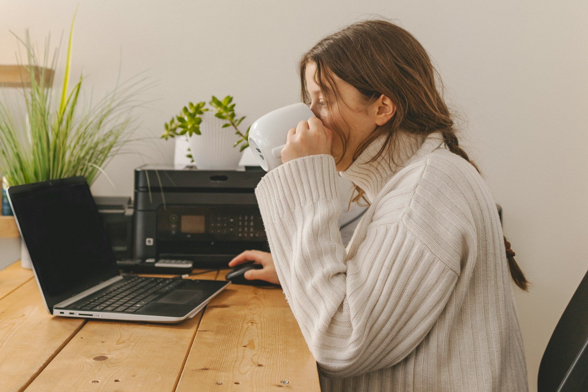 A woman is drinking a cup of coffee while using a laptop computer.