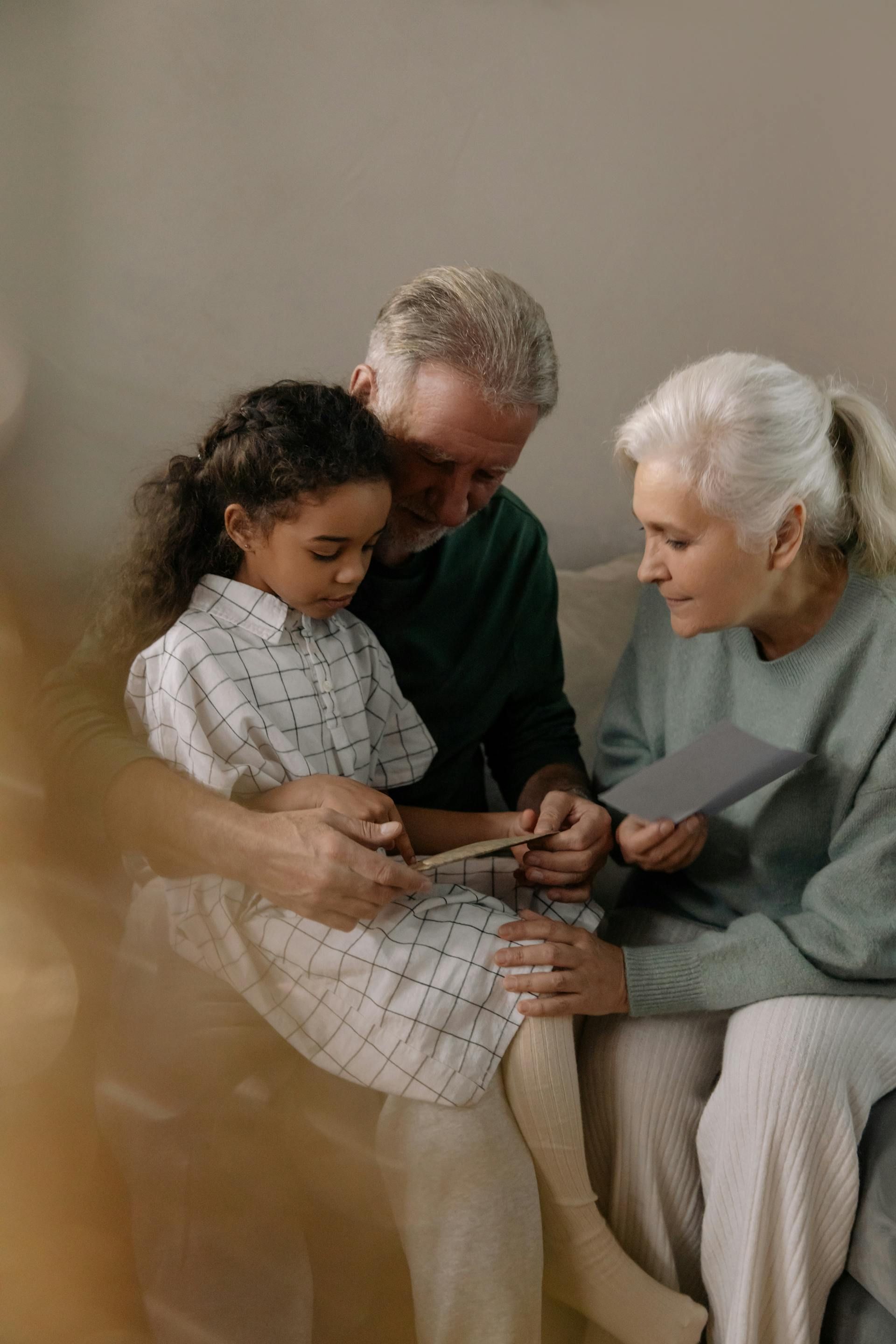 A little girl is sitting on a couch with her grandparents.