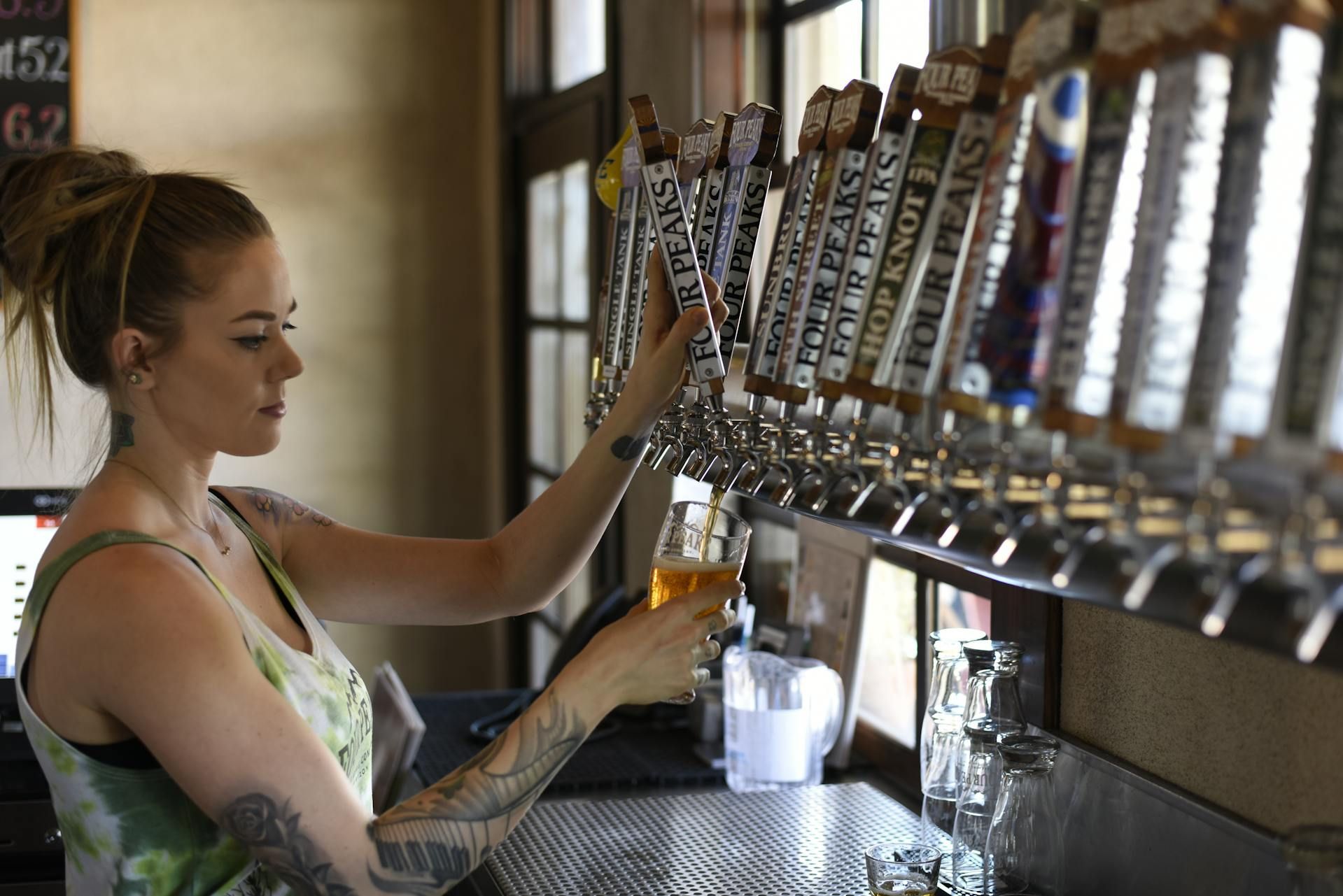 A woman is pouring beer from a tap at a bar.